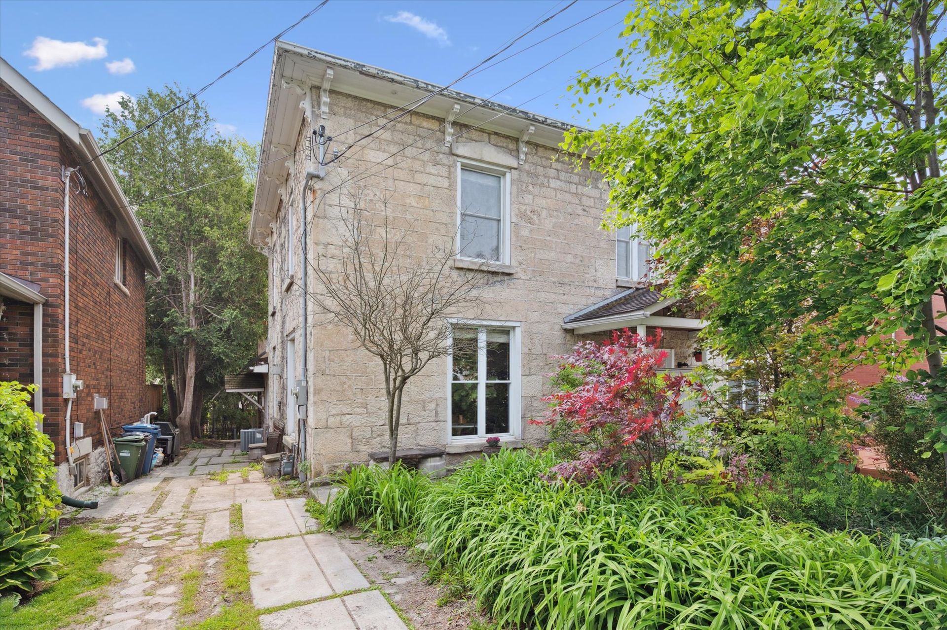 Stone house with a narrow garden path, lush greenery, and a flowering shrub under a clear blue sky
