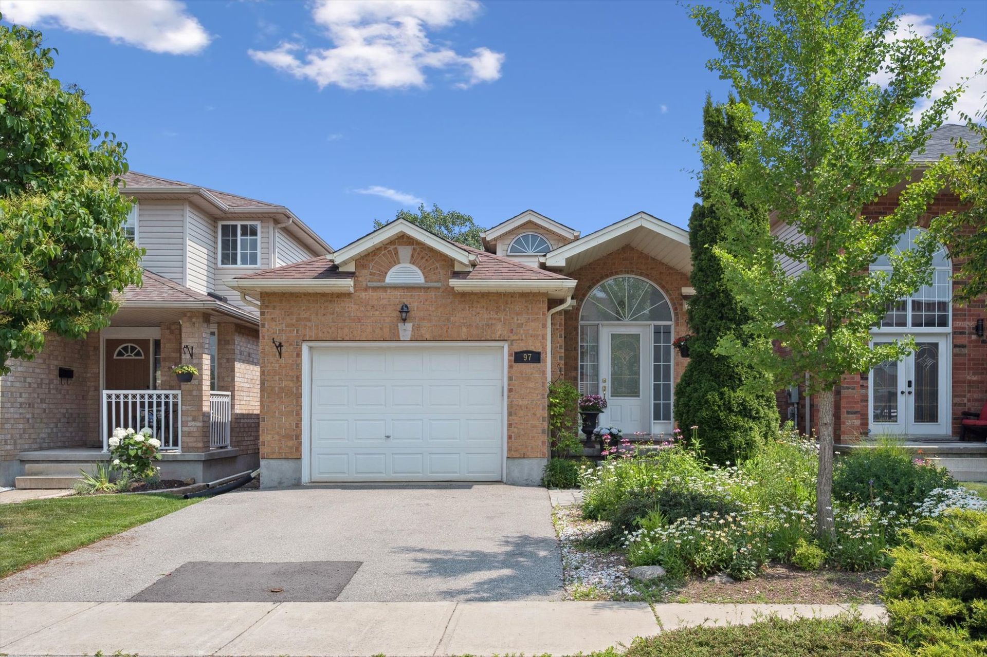 Suburban brick house with a two-car garage, front garden, and driveway under a blue sky