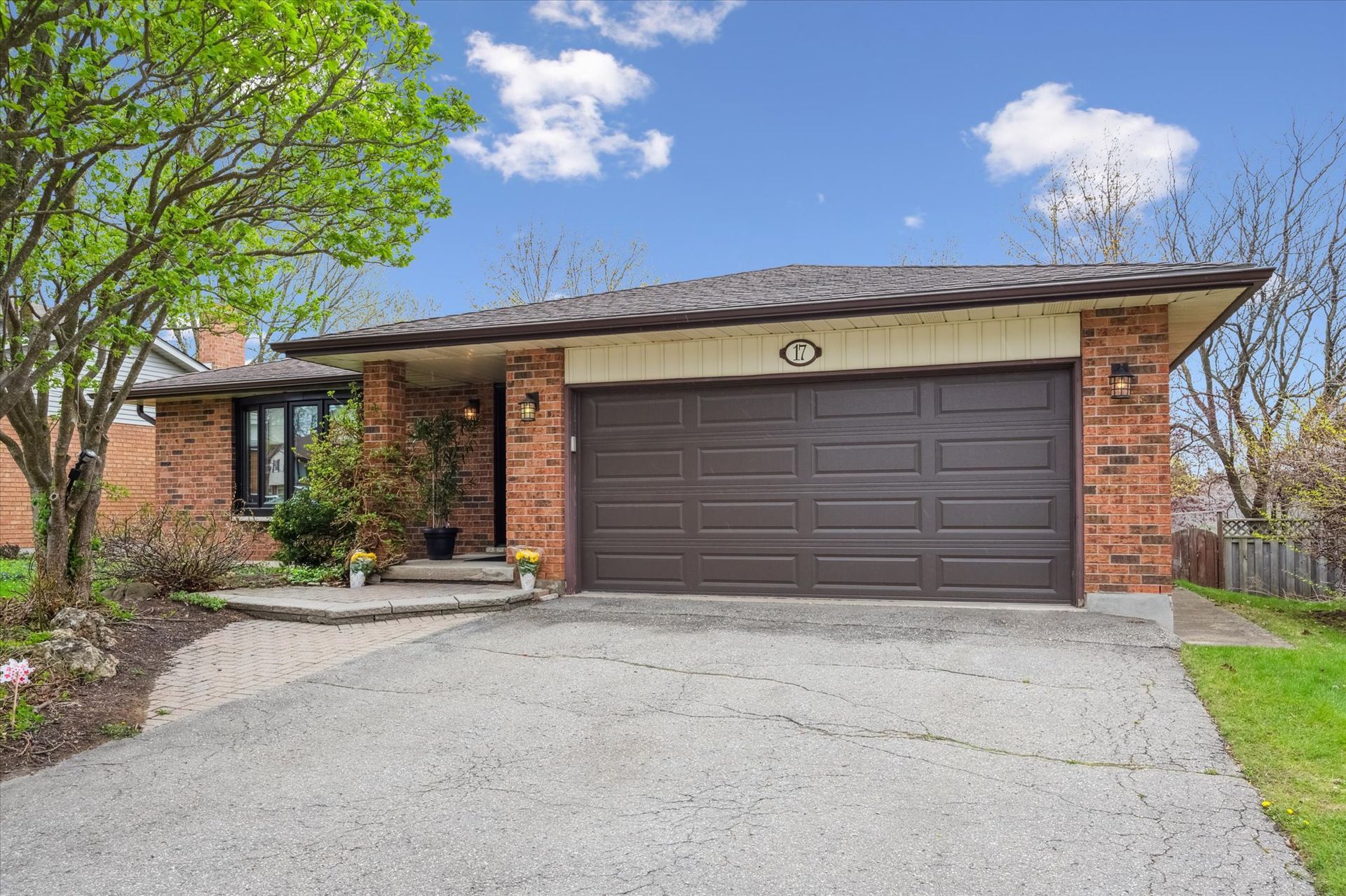 Single-story brick house with a two-car garage, driveway, and front yard trees