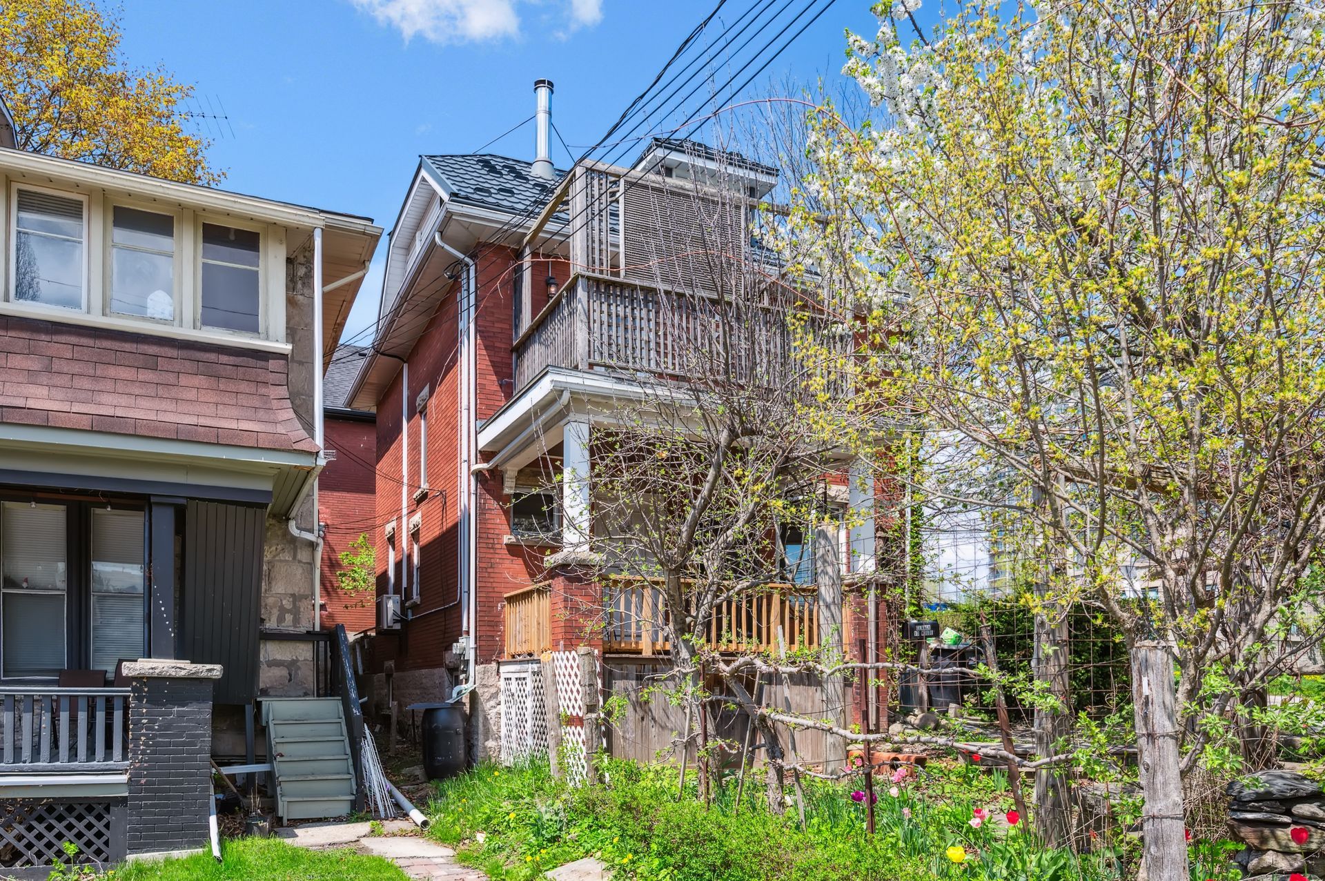 Brick row houses with balconies and a small garden under spring trees