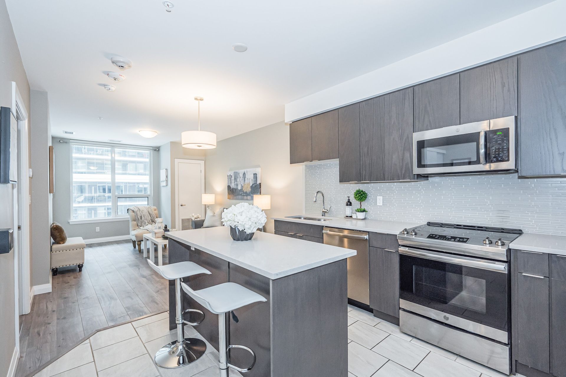 Modern kitchen with gray cabinets, stainless appliances, island seating, and bright open living area