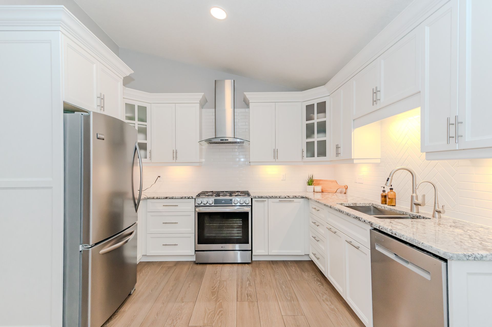 Bright modern white kitchen with stainless steel appliances, granite counters, and light wood flooring