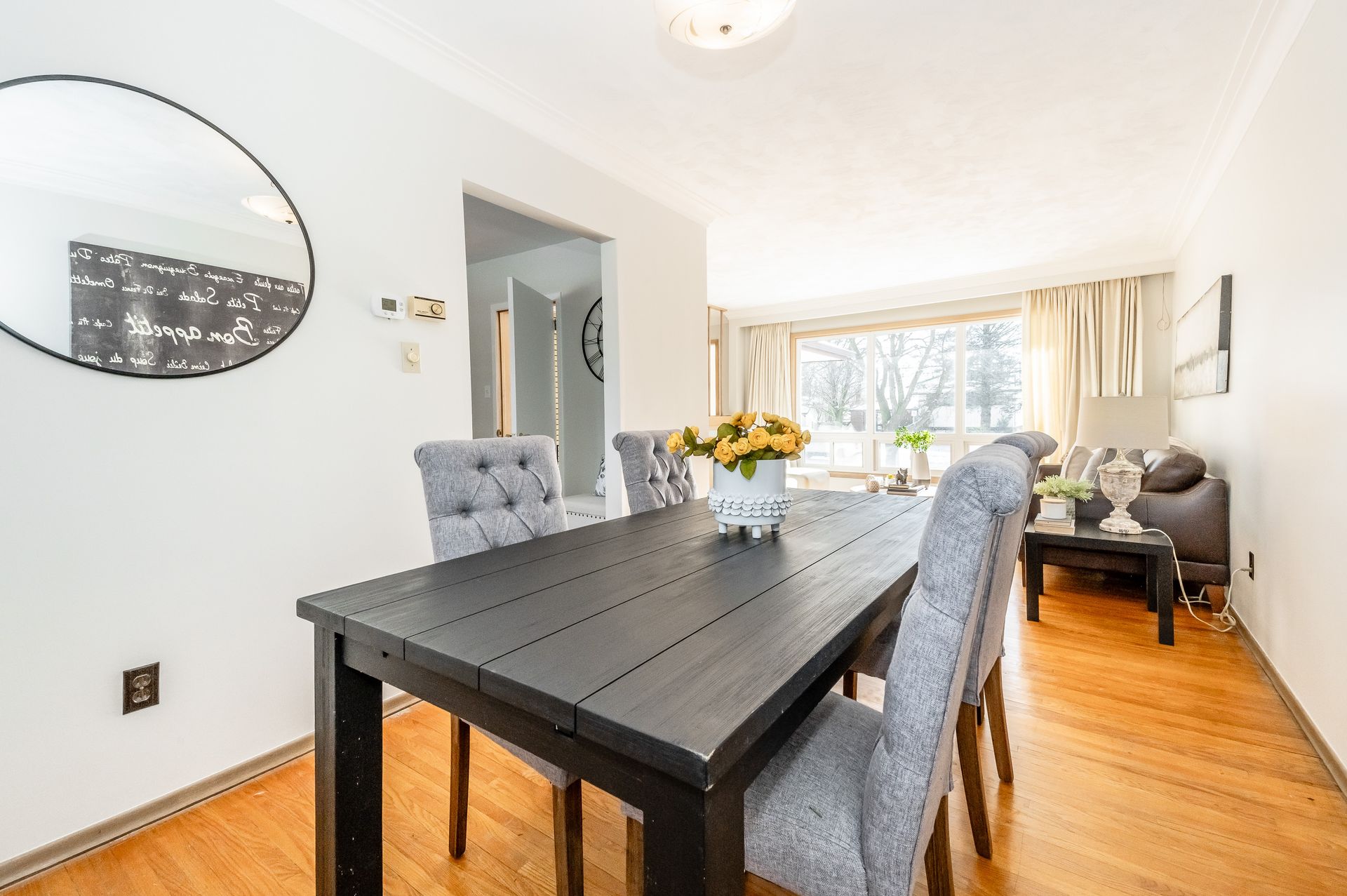 Bright dining room with a dark wood table, gray chairs, and a living area by large windows