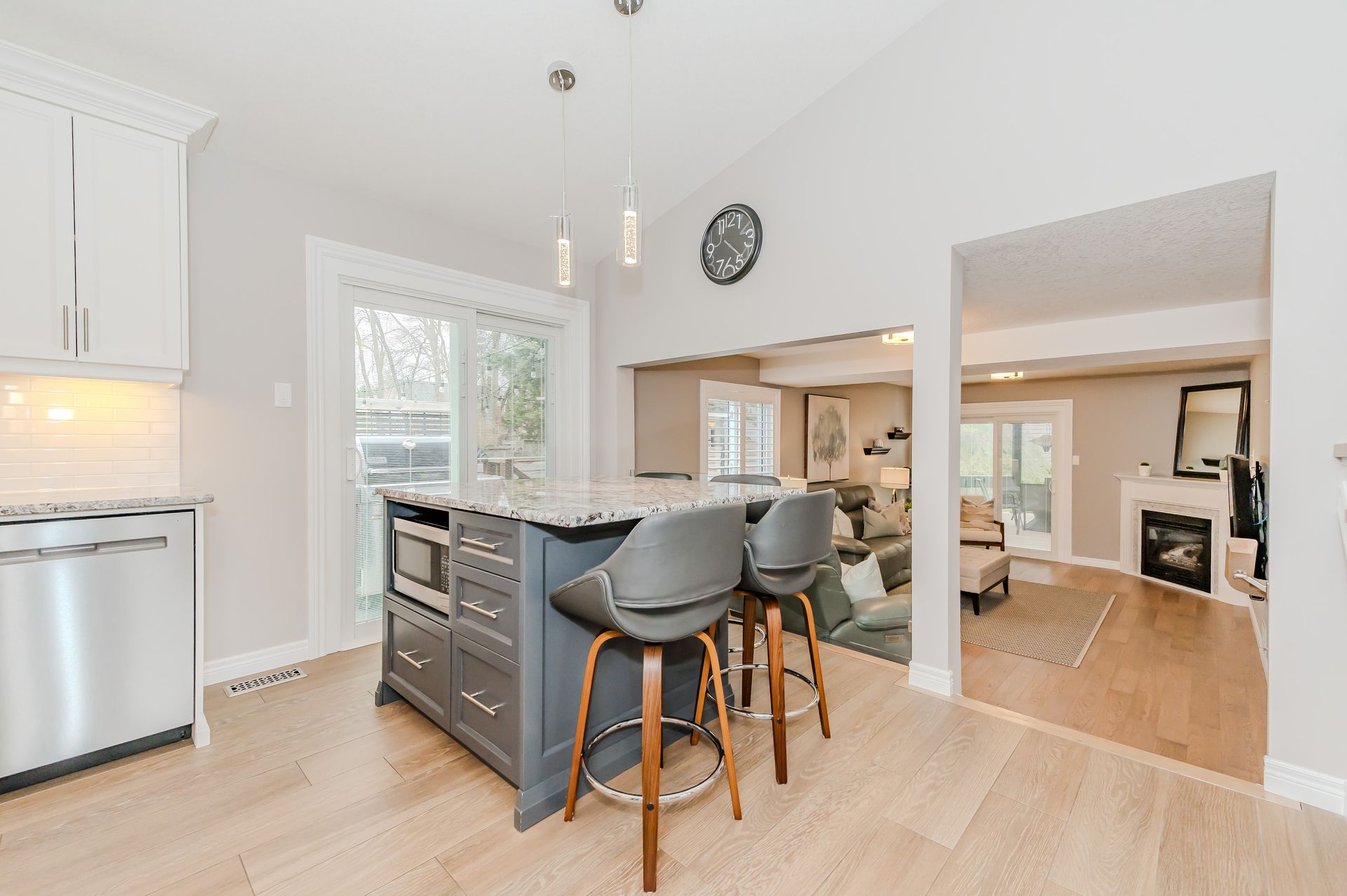 Bright kitchen with island and stools, stainless appliances, light wood floors, and open archway to dining room.