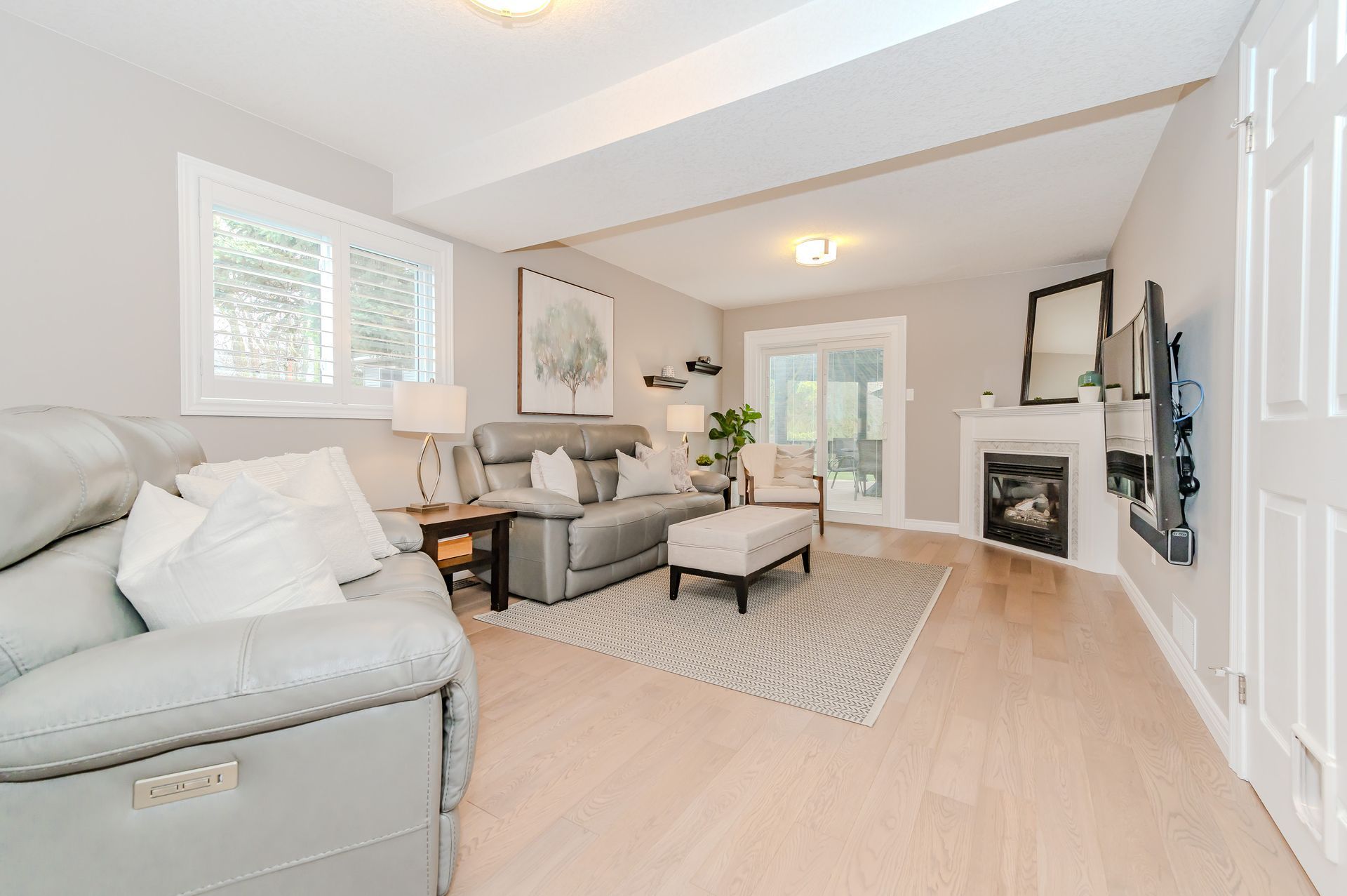 Bright living room with gray sectional, chairs, fireplace, rug, and light wood floors