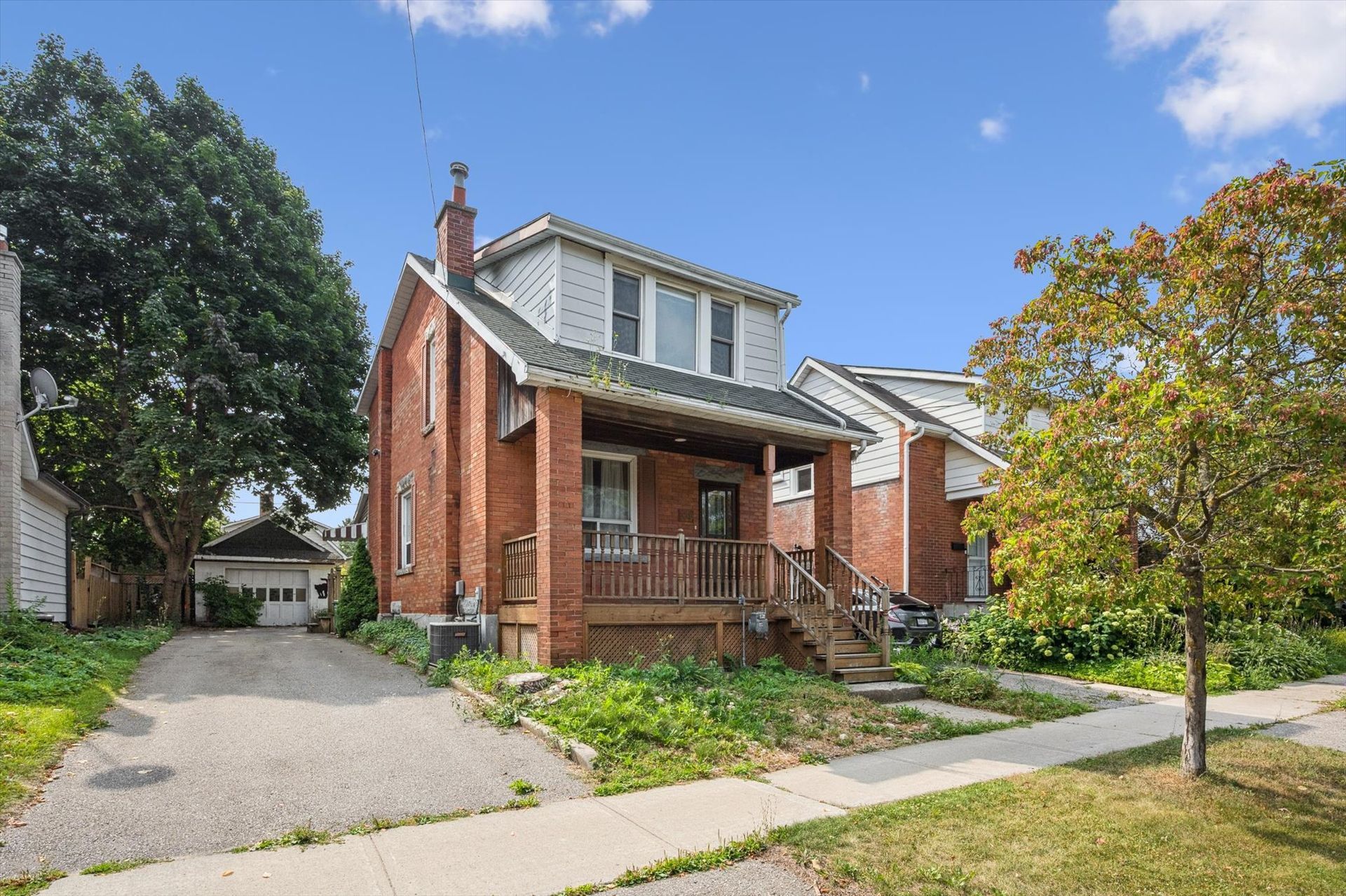 Red brick house with front porch, driveway, and green lawn on a sunny day