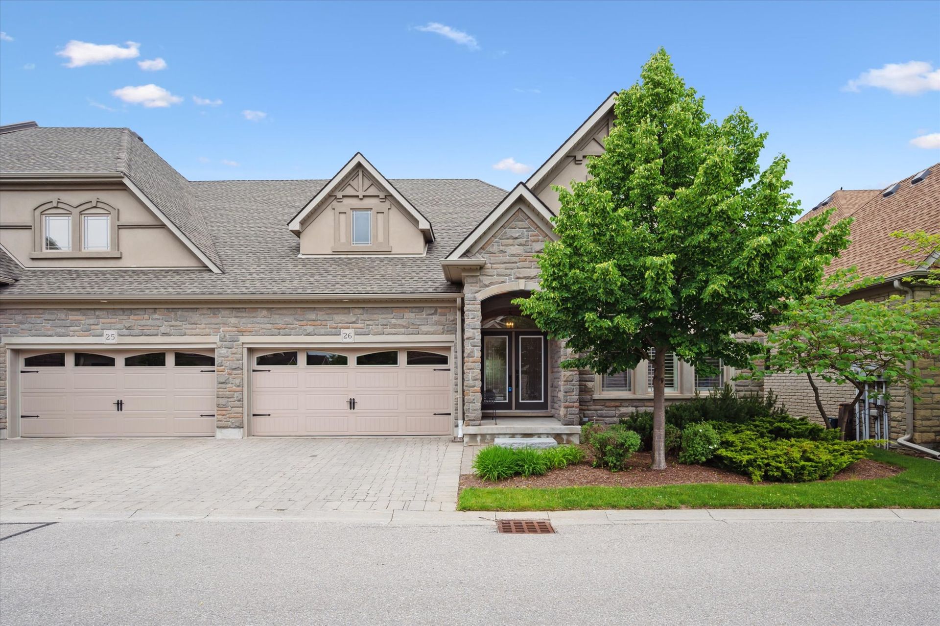 Suburban house exterior with three-car garage, stone facade, and a tree-lined front yard