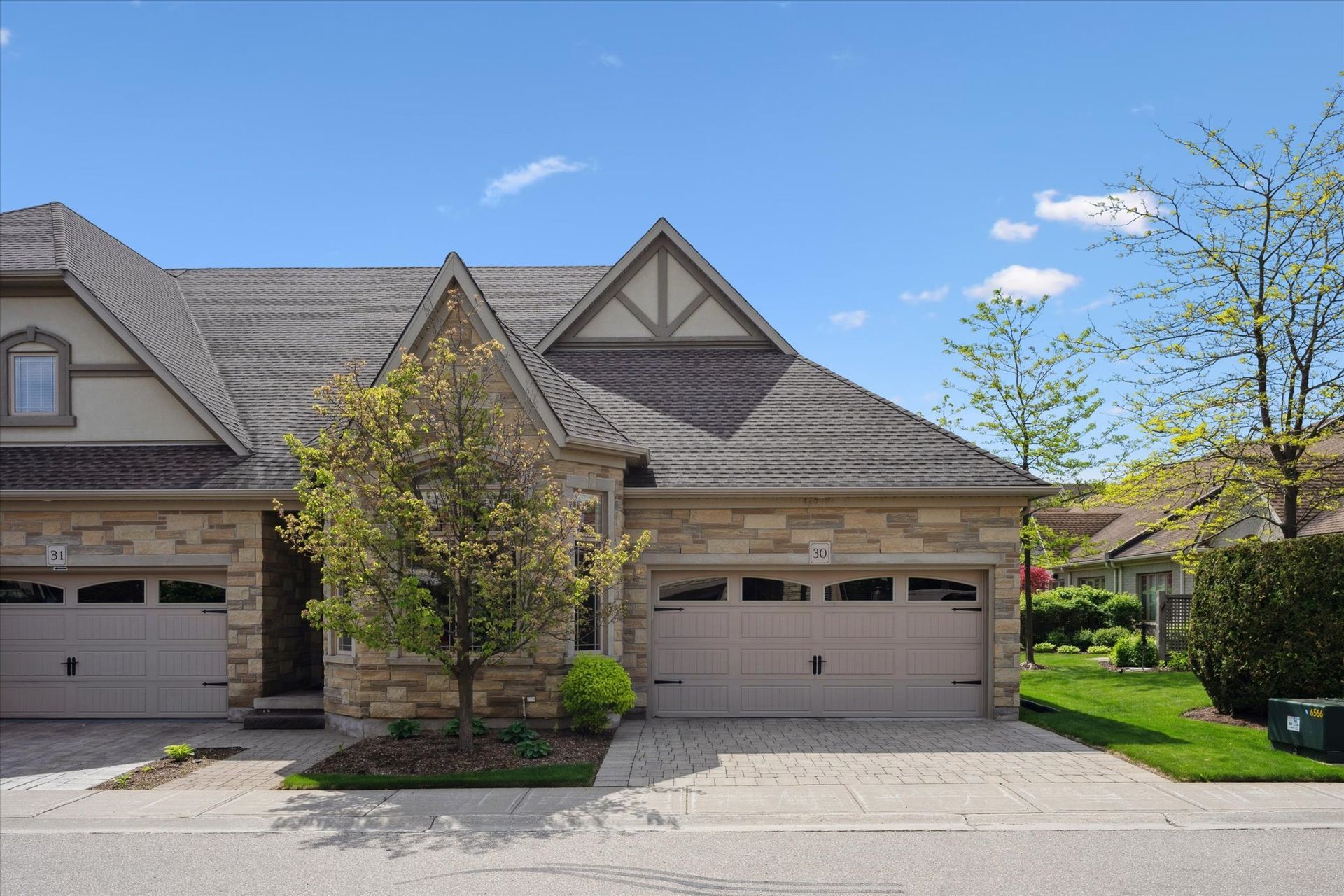 Suburban townhouse exterior with two garage doors, stone facade, and a small tree in front