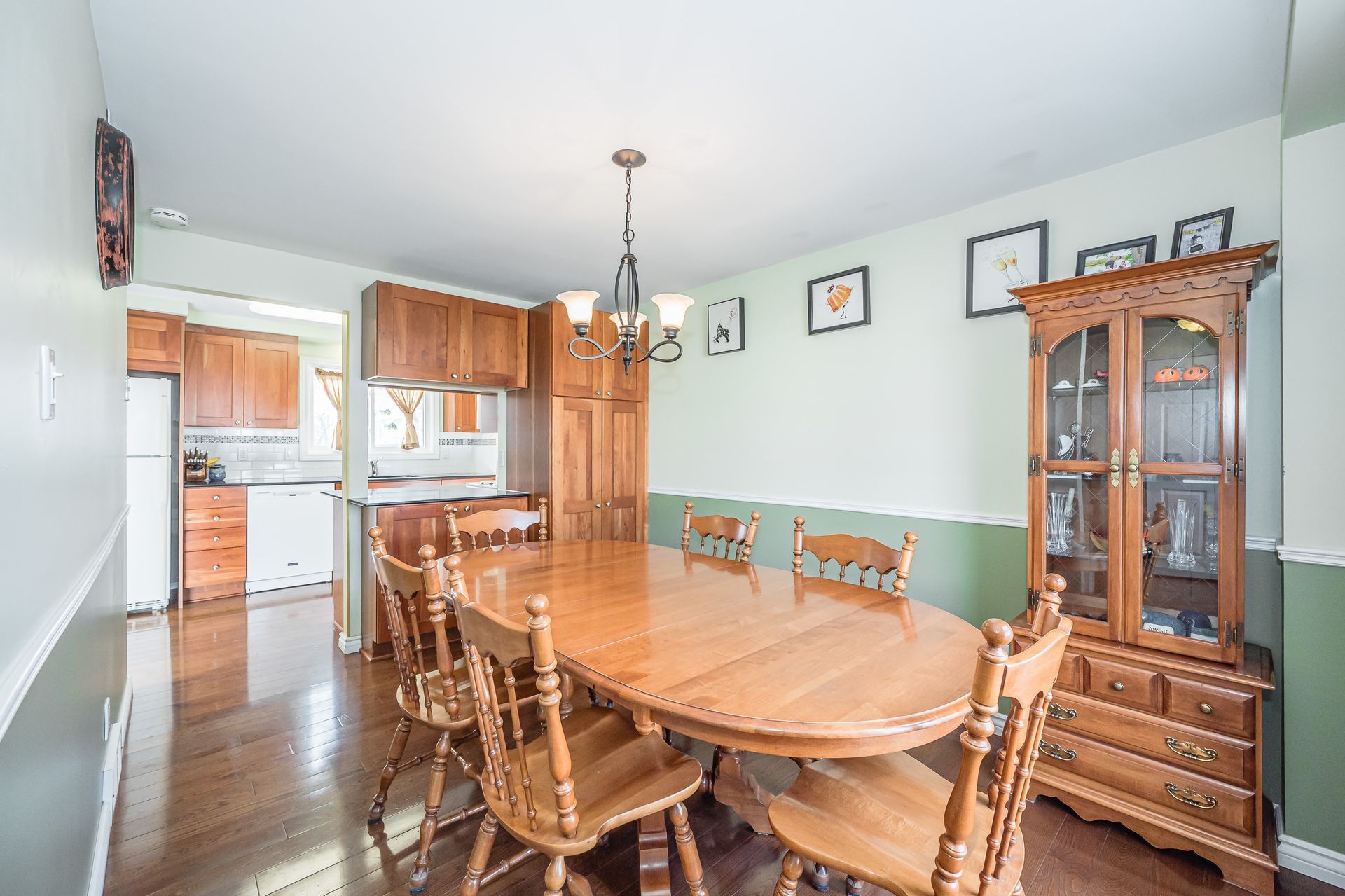 Dining room with wooden table and china cabinet, open to a kitchen in the background.