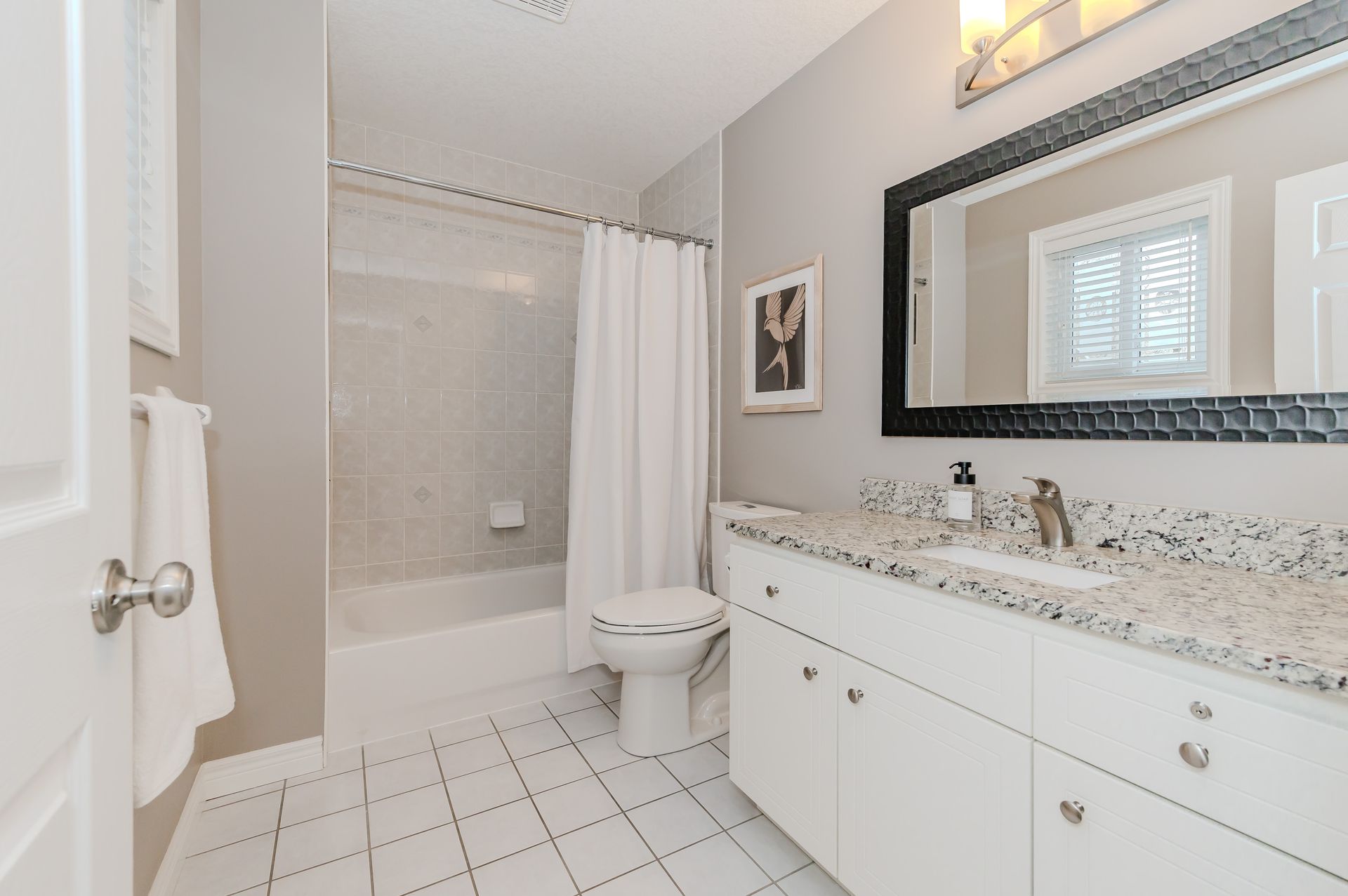 Bright white bathroom with shower, toilet, and vanity with large mirror and tiled floor.