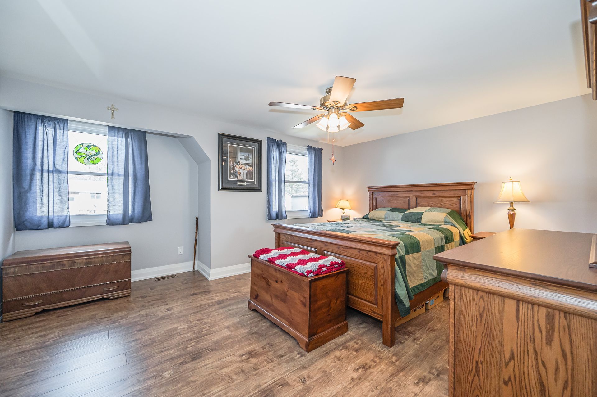 Spacious bedroom with wood bed, dresser, ceiling fan, and blue curtains in gray walls