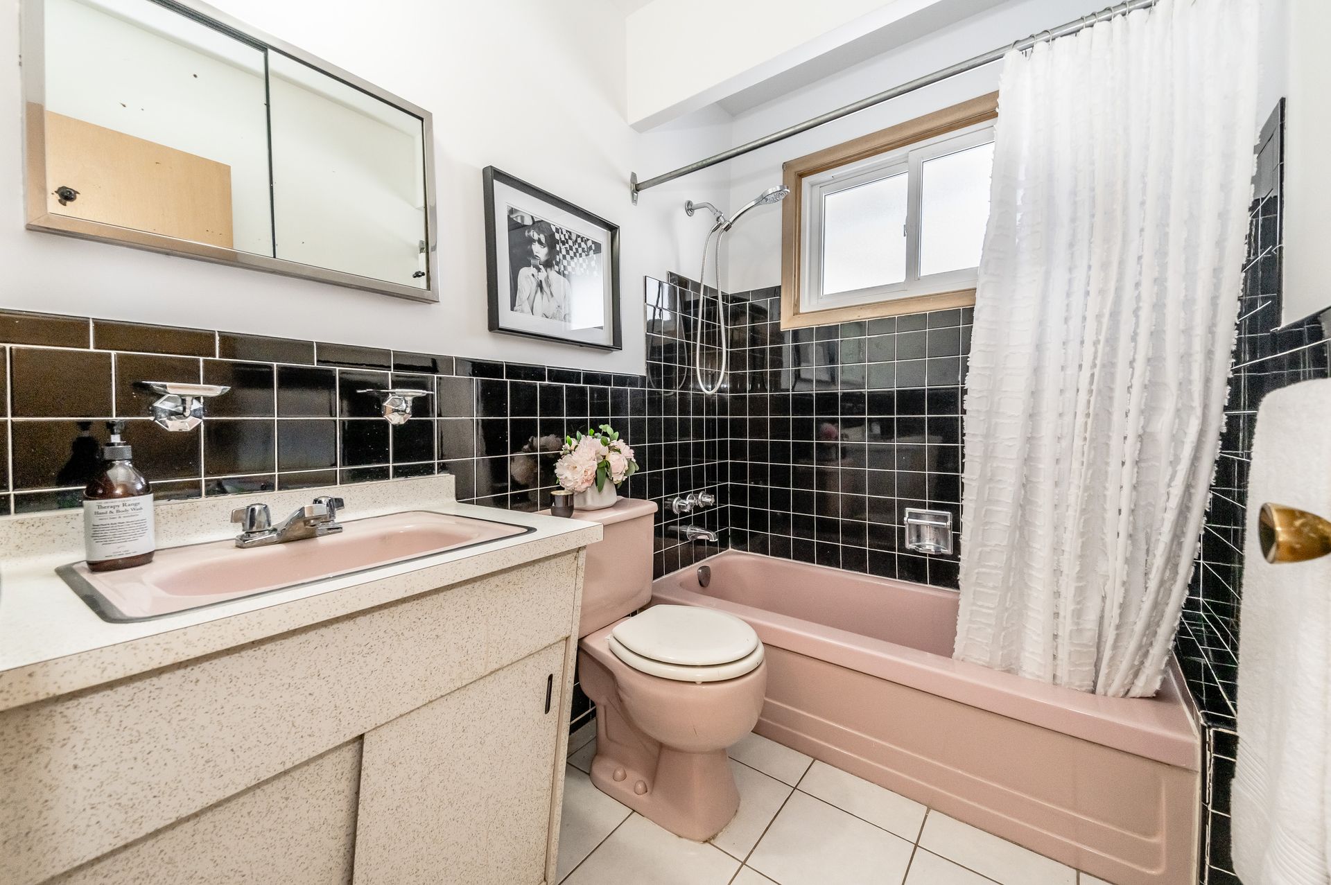 Bright bathroom with pink vanity, black tile, and a white shower curtain over a tub.