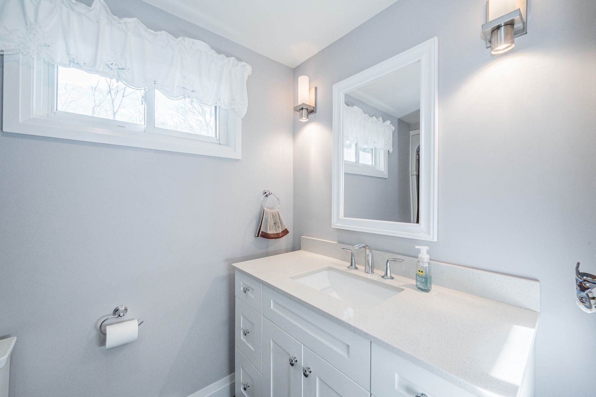 Bright white bathroom vanity with mirror, window, and wall sconces