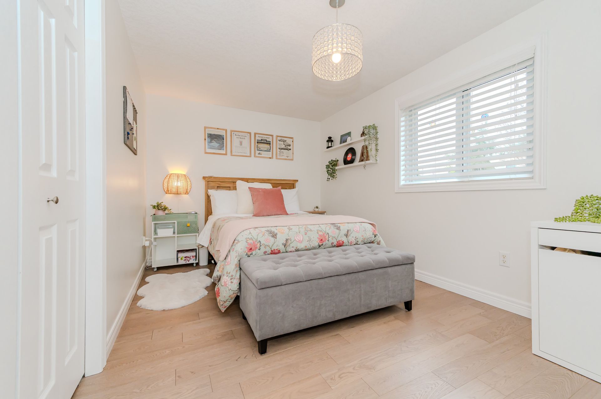 Bright bedroom with a gray bench, white walls, a window with blinds, and a bed with floral bedding