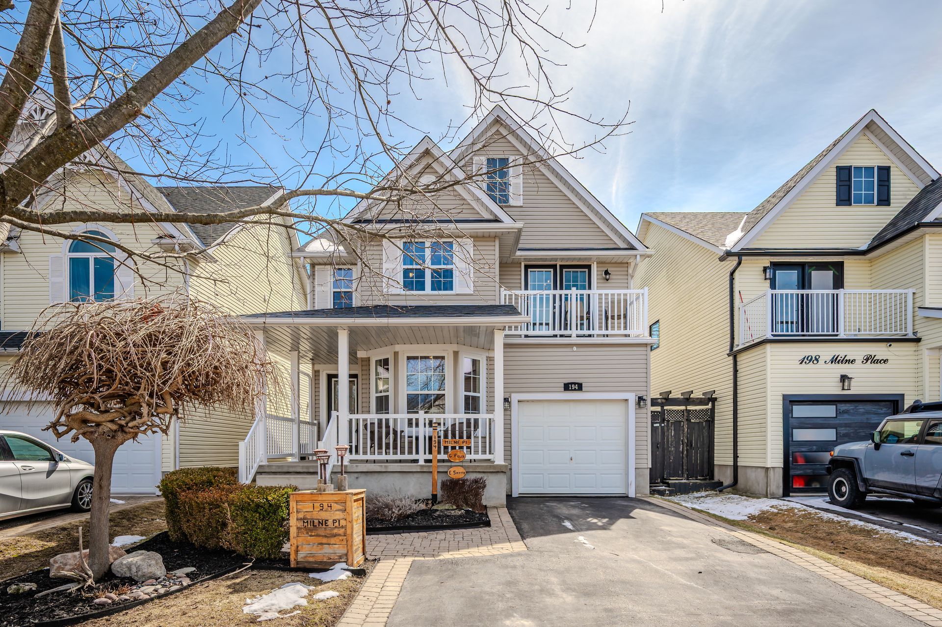 Suburban townhouse with white garage, porch, parked car, and snowy driveway on a sunny day