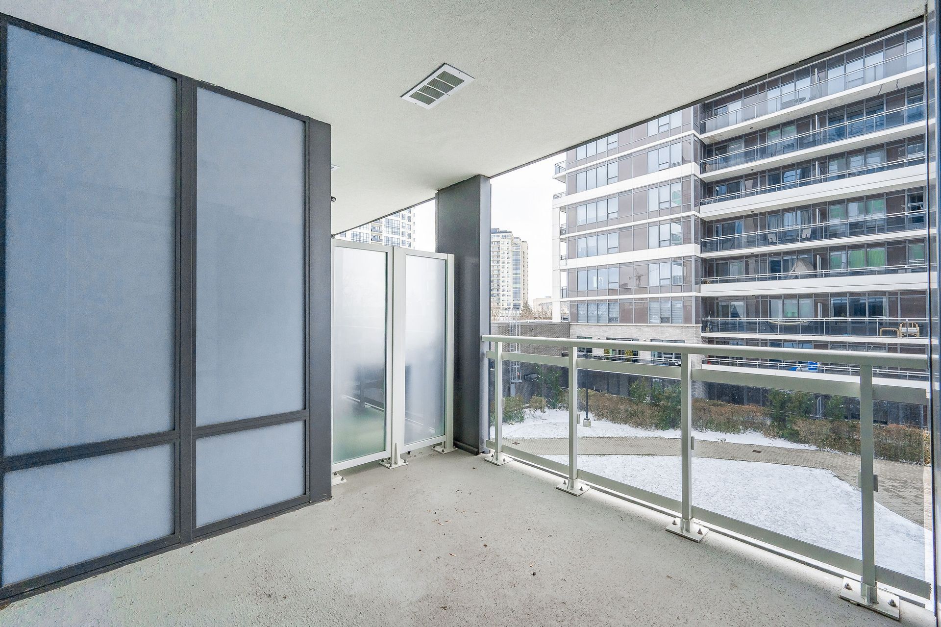 Empty modern balcony with glass railing overlooking an apartment building and street.