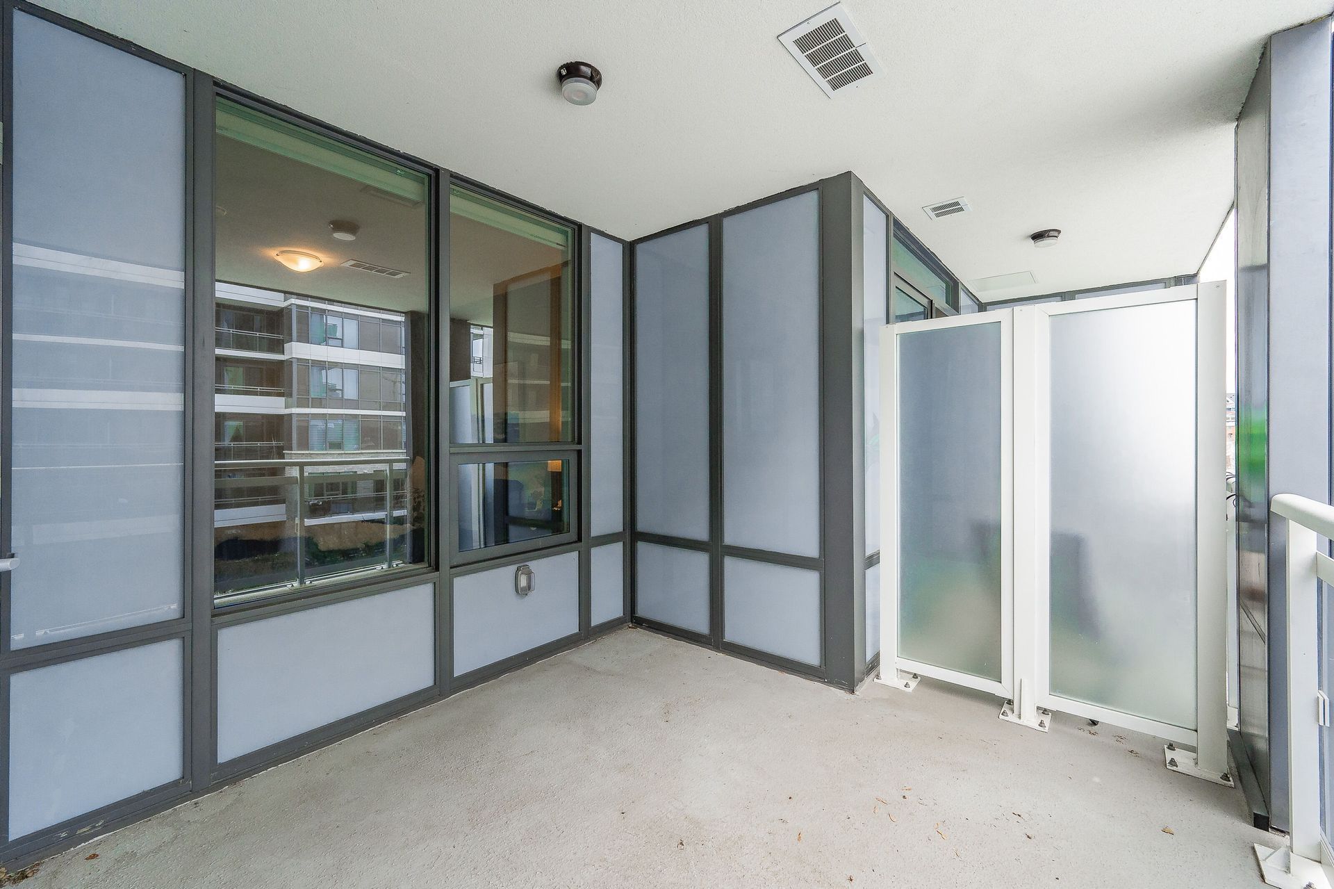Empty modern balcony with frosted glass panels and gray walls beside a building entry.