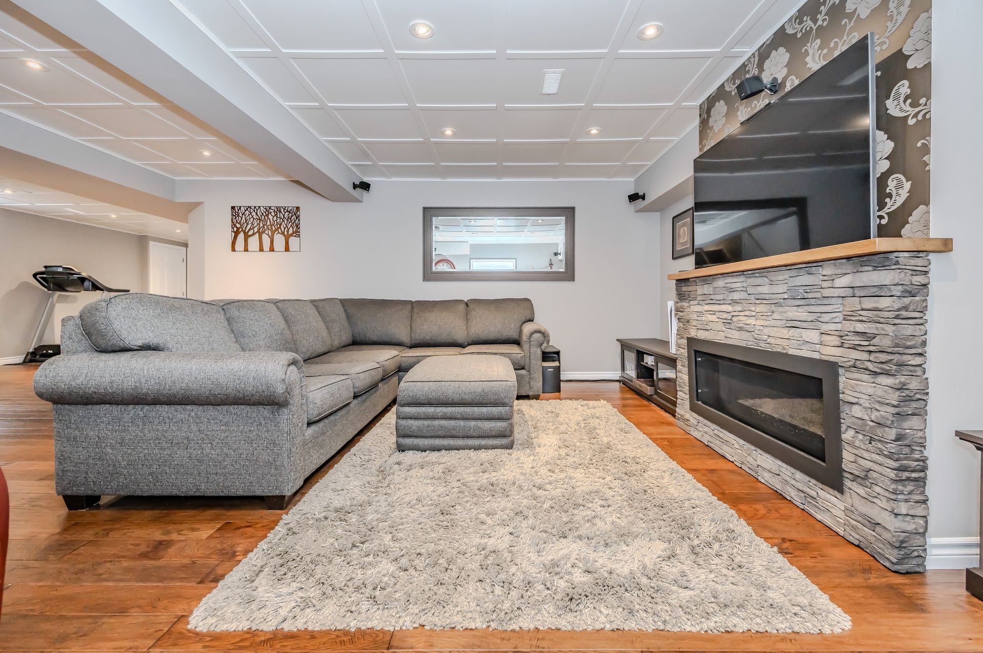 Spacious living room with gray sectional, stone fireplace, and large rug on hardwood floors