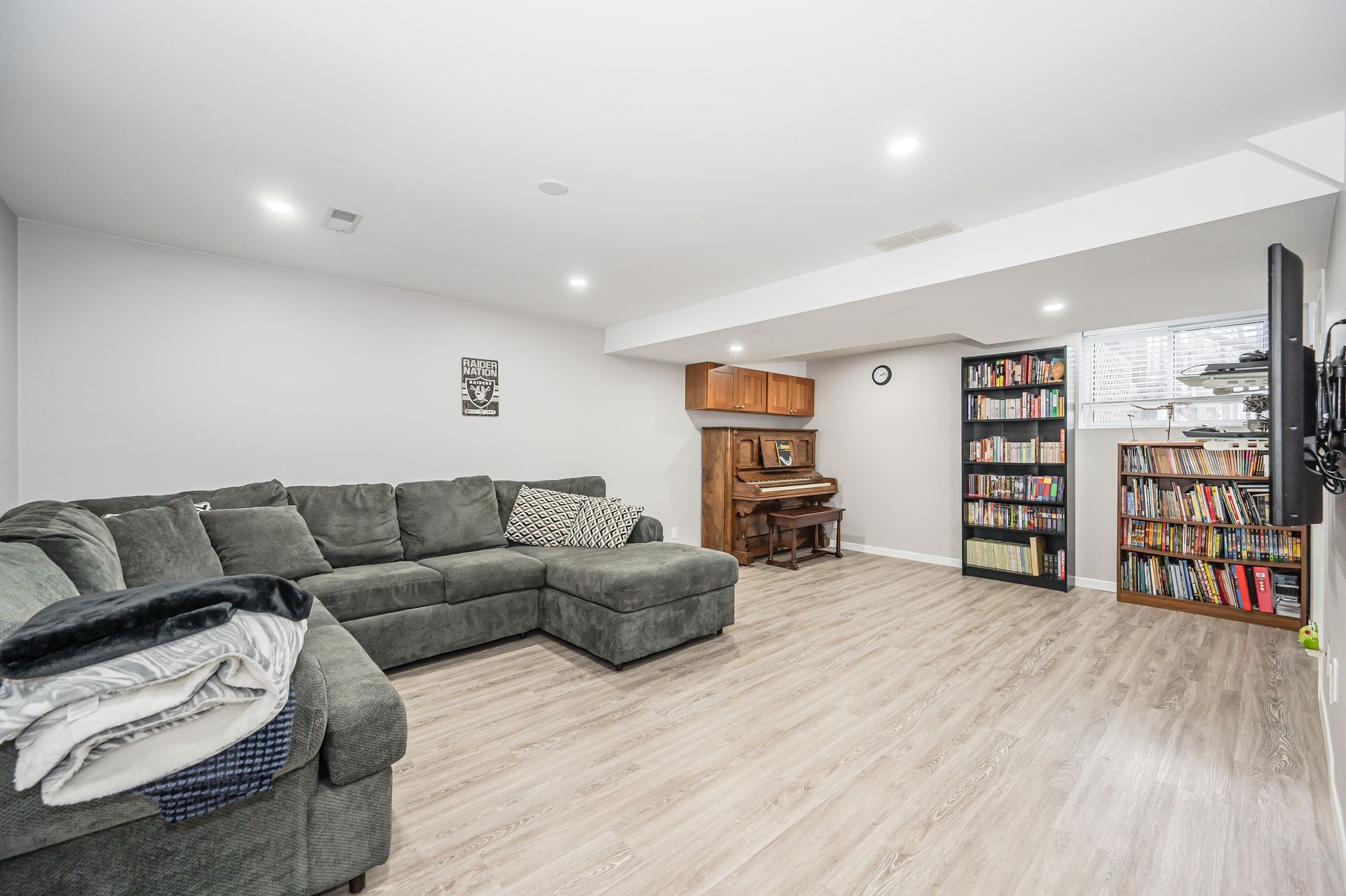Bright basement family room with gray sectional sofa, wood floor, shelves, and bookshelves