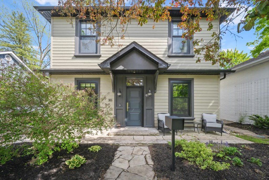 Two-story gray house with a front porch, stone walkway, and landscaped yard.