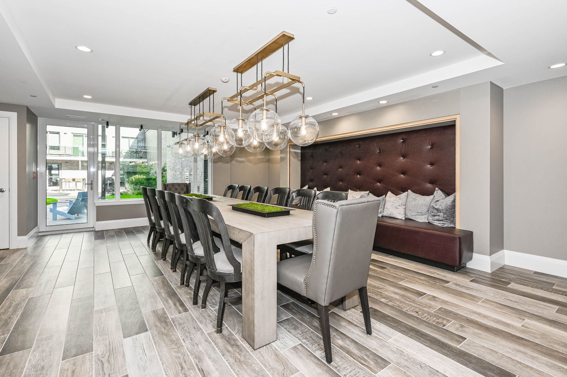 Modern dining room with long table, upholstered chairs, chandelier, and tufted wall bench seating