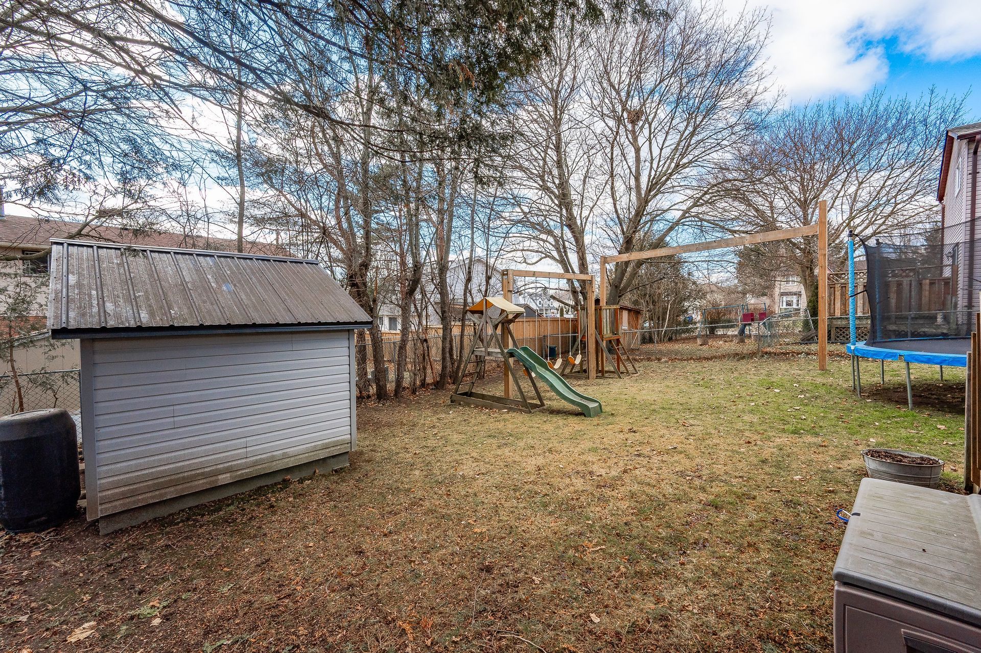 Backyard with shed, bare trees, and a small playset beside a trampoline