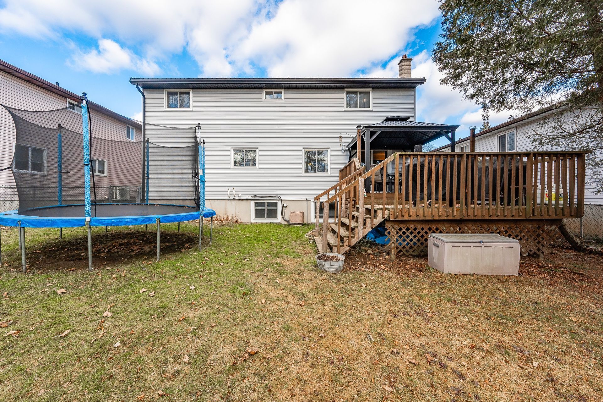 Backyard with trampoline, wooden deck stairs, and white two-story house under a blue sky