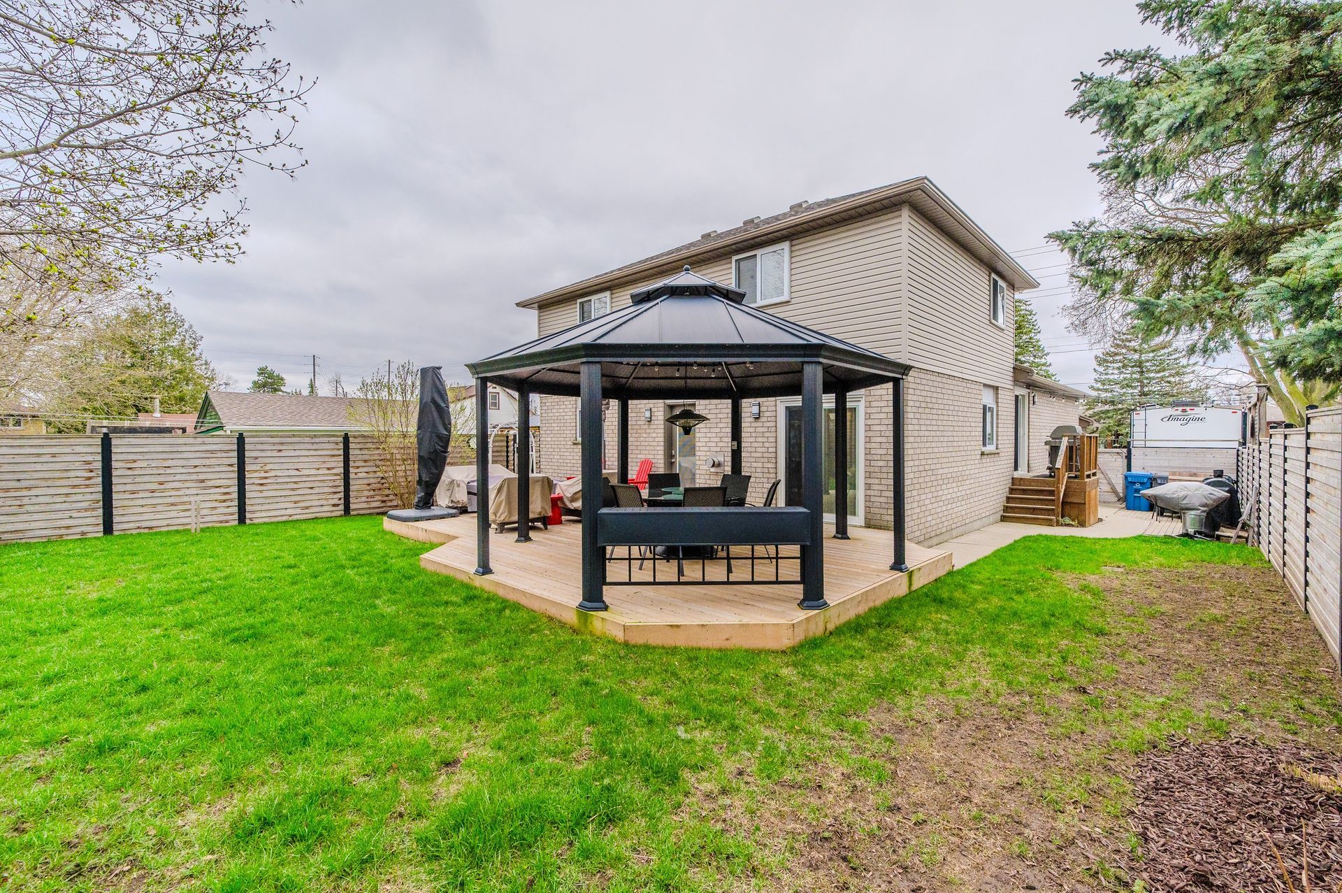 Backyard patio with black gazebo, seating, and a two-story house beside a green lawn