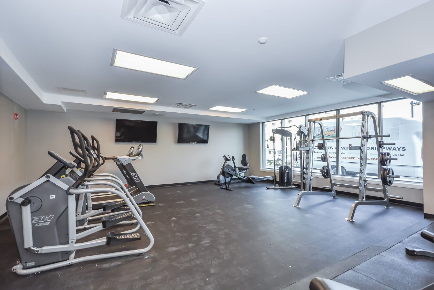 Modern gym with treadmills, exercise bikes, wall TVs, mirrors, and large windows