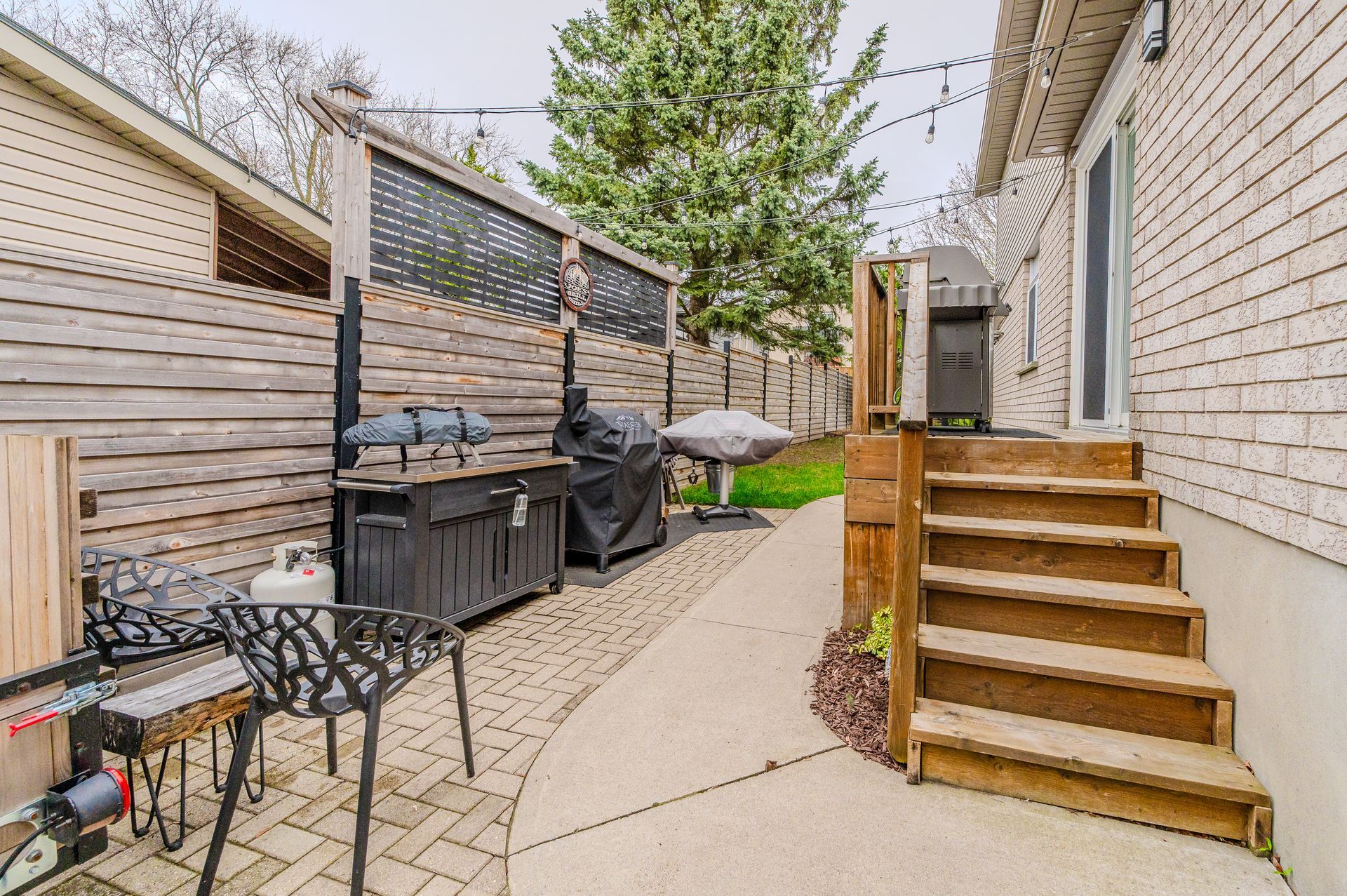 Narrow backyard walkway with wooden steps, patio furniture, and privacy fencing between two houses