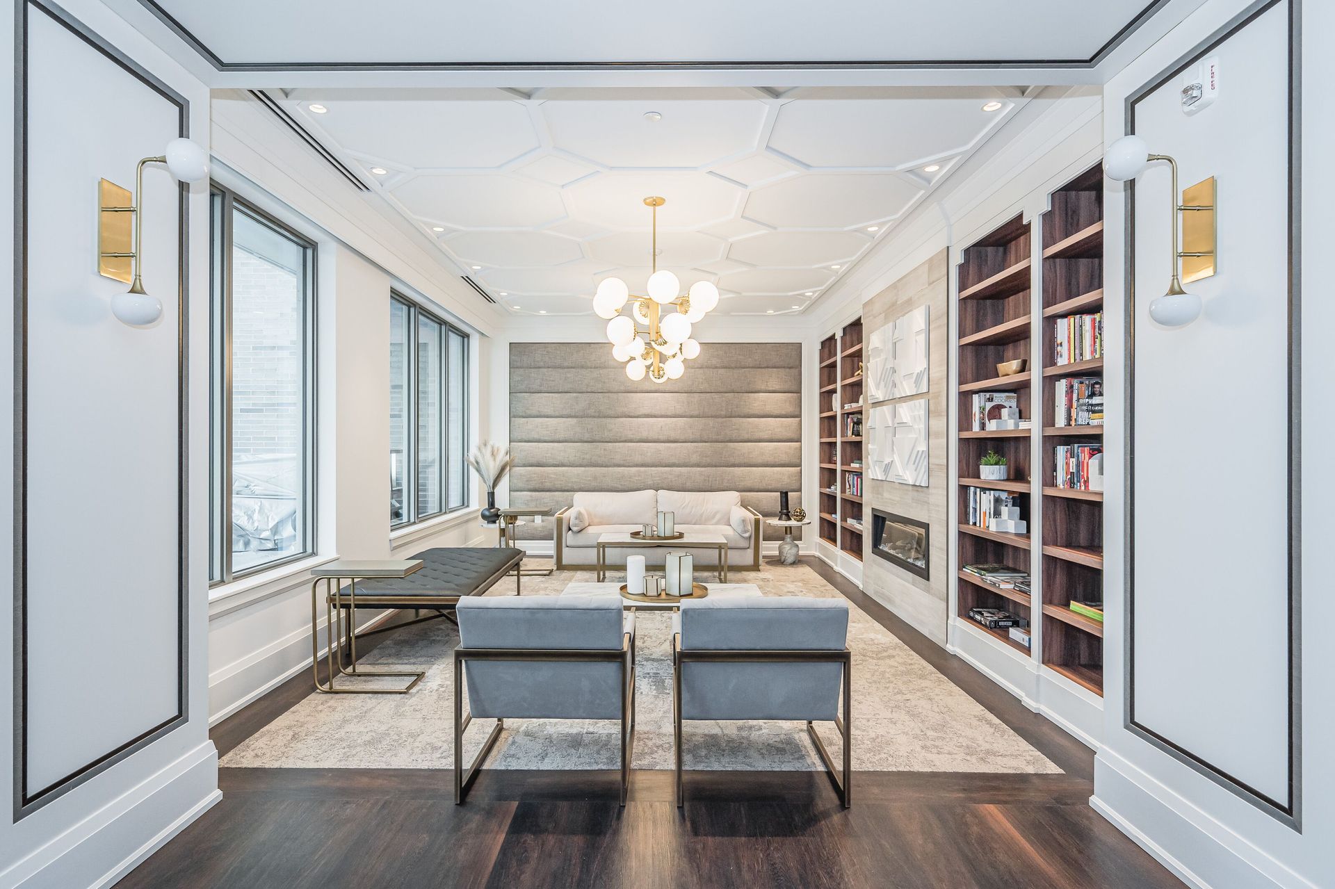 Elegant modern living room with white paneled walls, gray seating, bookshelves, and a chandelier