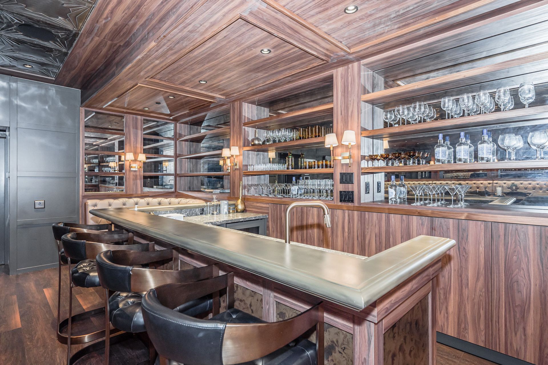Warm wood bar interior with shelves of glassware, mirrored back wall, and black stools