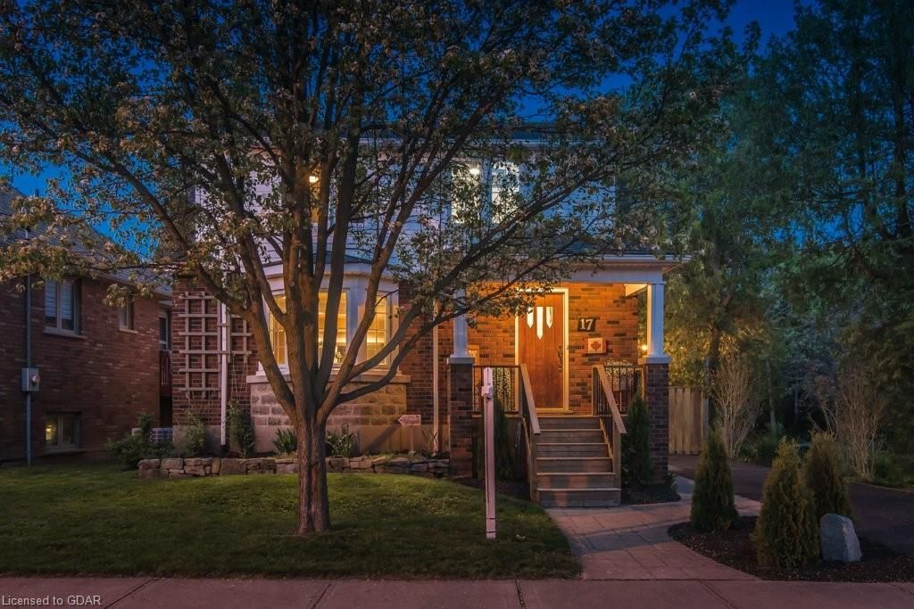 Brick house at dusk with lit front porch, steps, trees, and a sidewalk in front