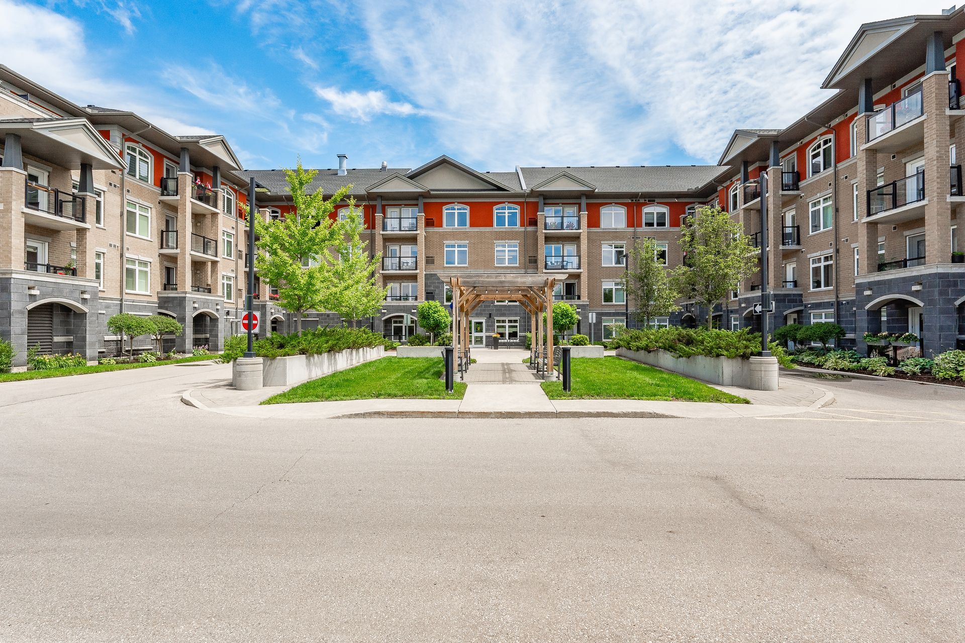 Modern apartment courtyard with landscaped walkways, trees, and brick buildings under a blue sky