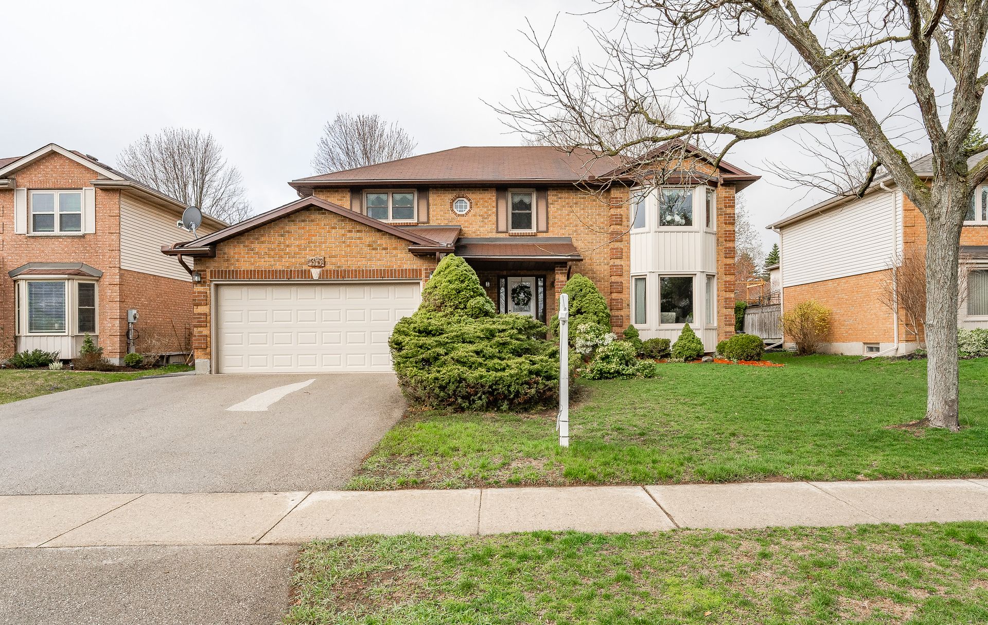 Suburban brick two-story house with a two-car garage, front lawn, and tree-lined sidewalk