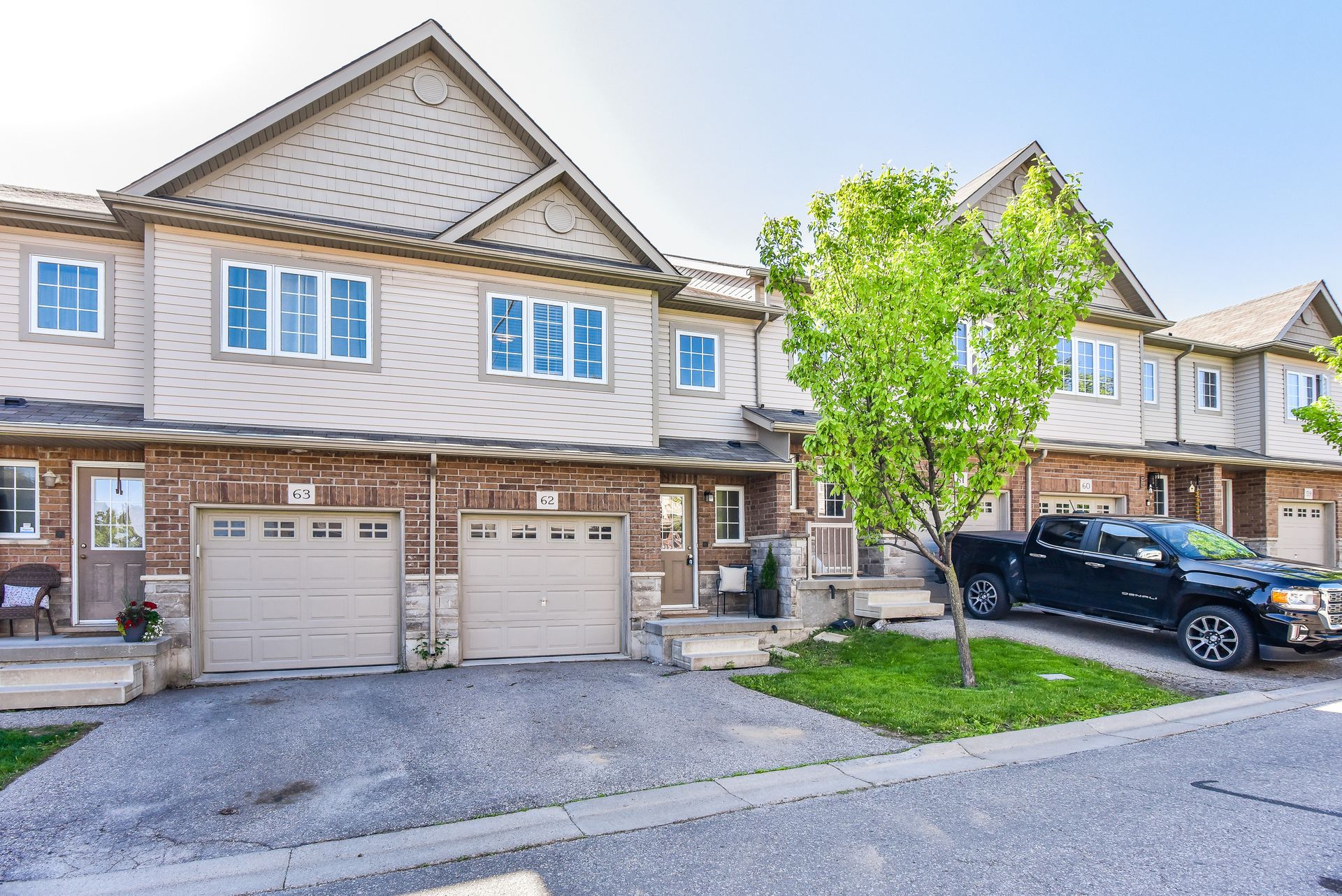 Row of beige townhouses with attached garages, a tree, and a black SUV parked outside