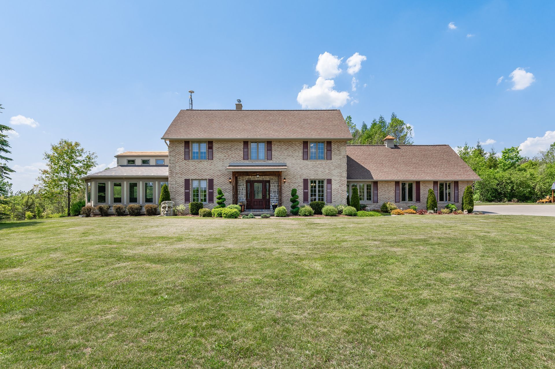 Large rustic stone house with a shingled roof and wide green lawn under a clear blue sky