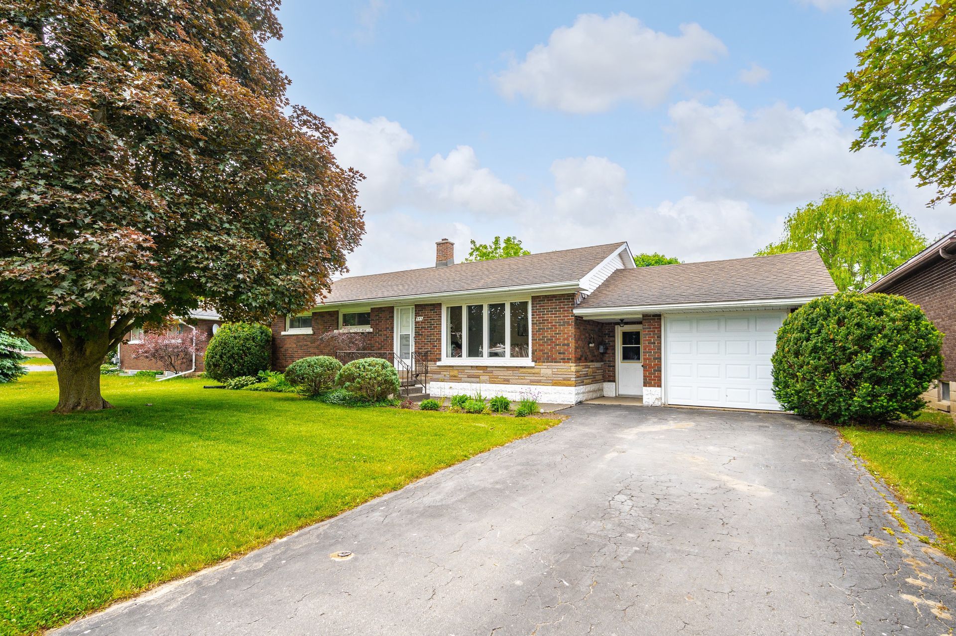 Suburban house with white garage, brick facade, and a driveway bordered by green lawn and trees