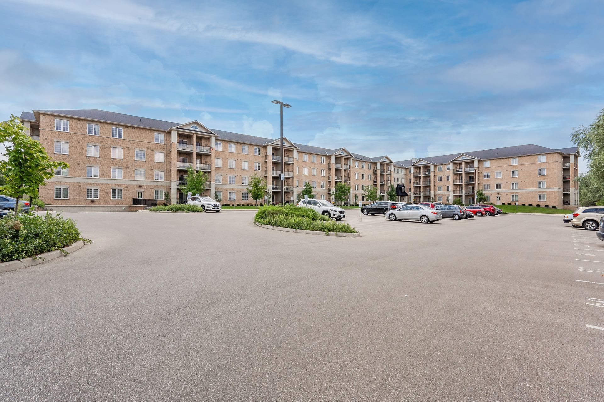 Apartment complex with parked cars and a large gravel lot under a blue sky
