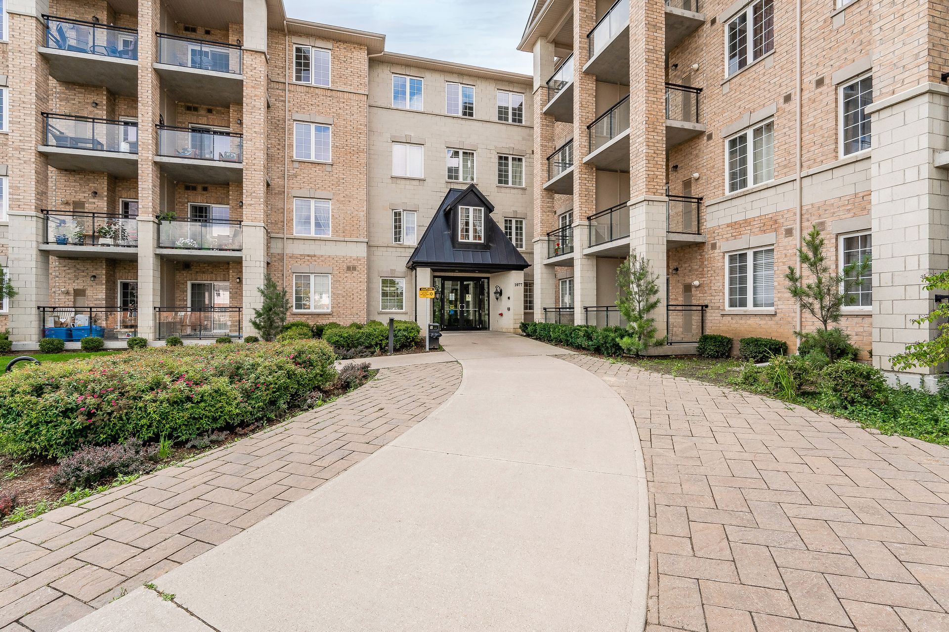 Courtyard path between brick apartment buildings leading to a dark entrance with flower beds on both sides