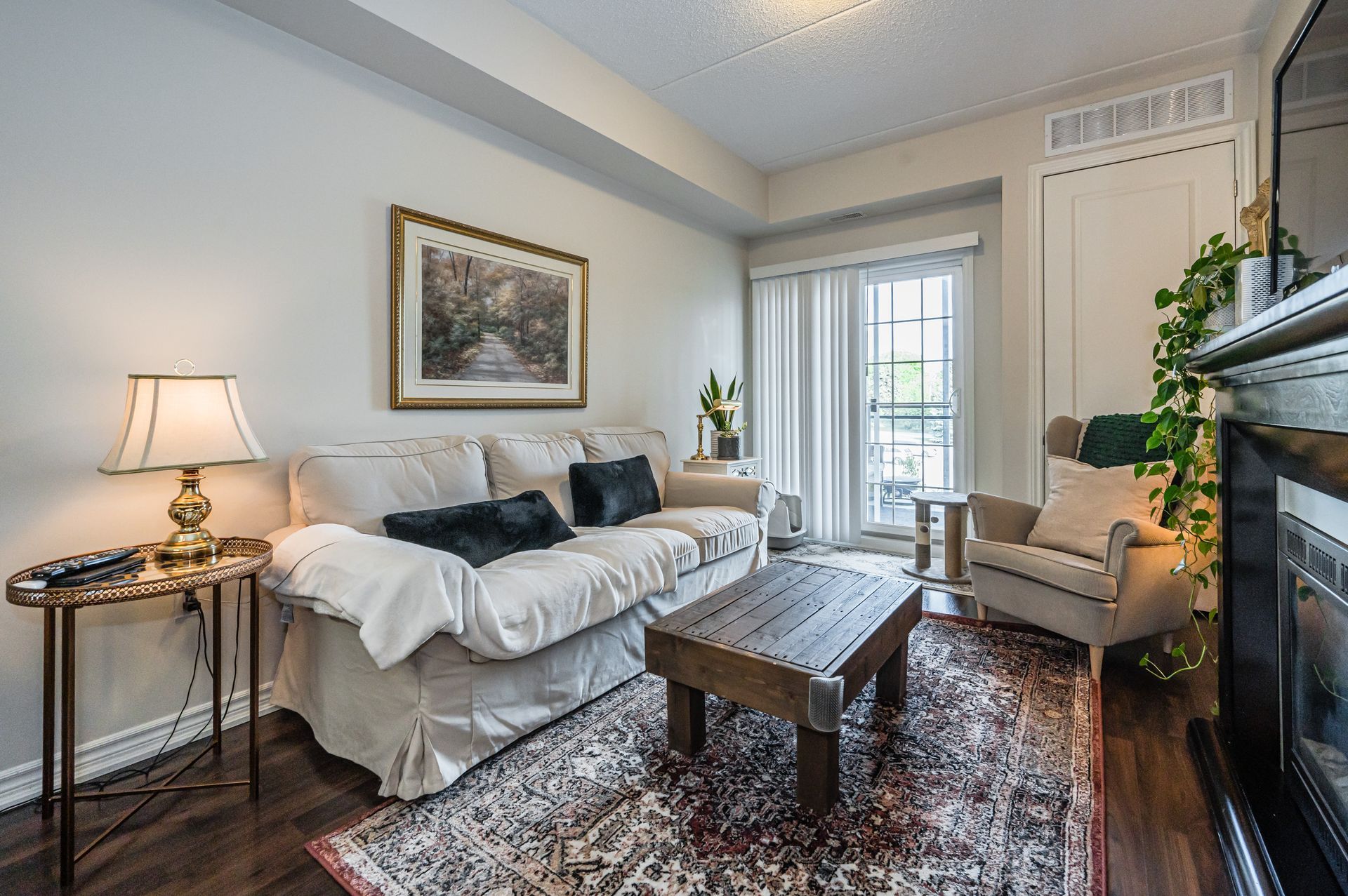 Cozy living room with white sofa, patterned rug, coffee table, lamp, and fireplace beside a bright window.