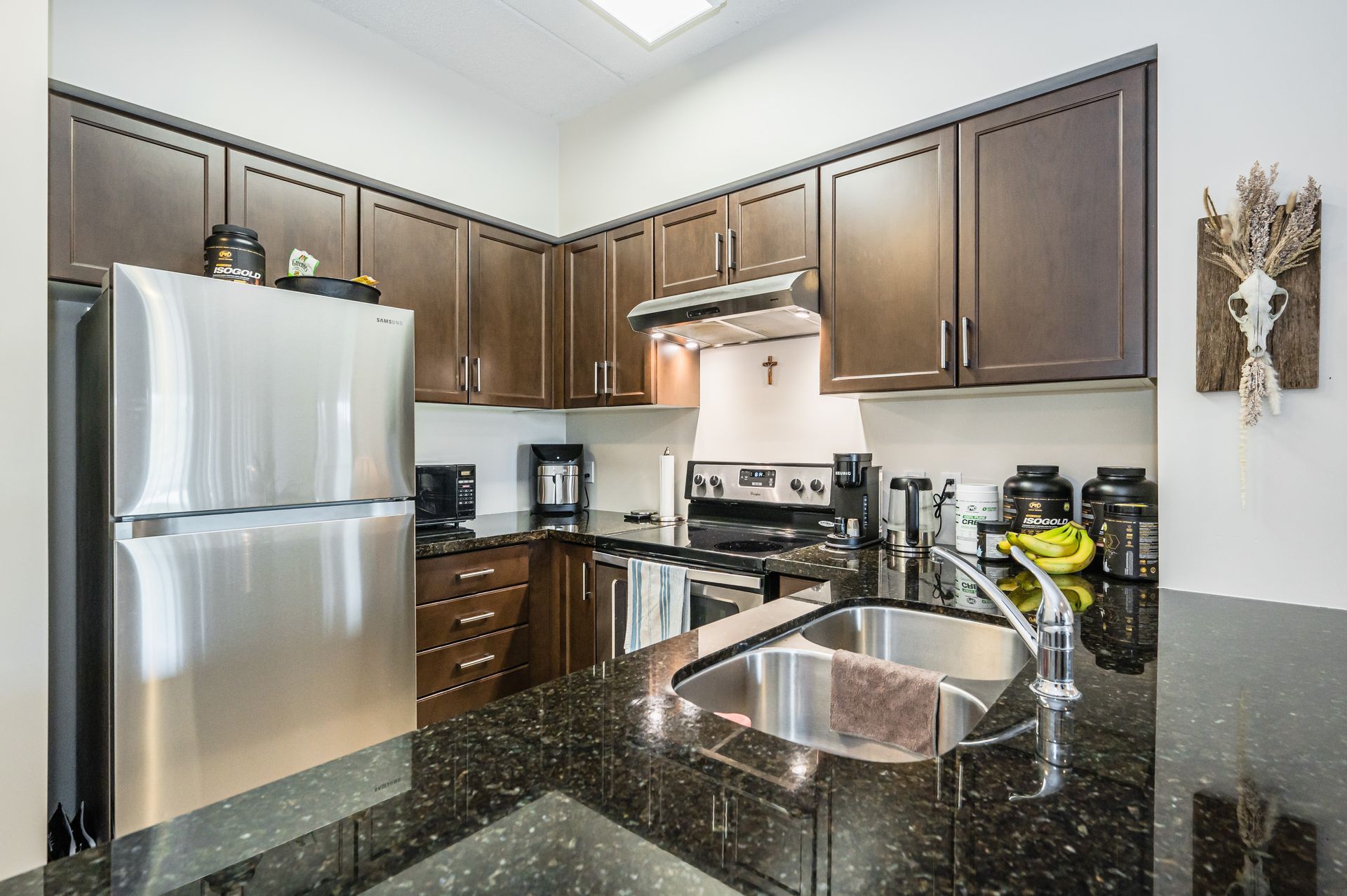 Modern kitchen with stainless steel appliances, dark wood cabinets, and black granite countertops
