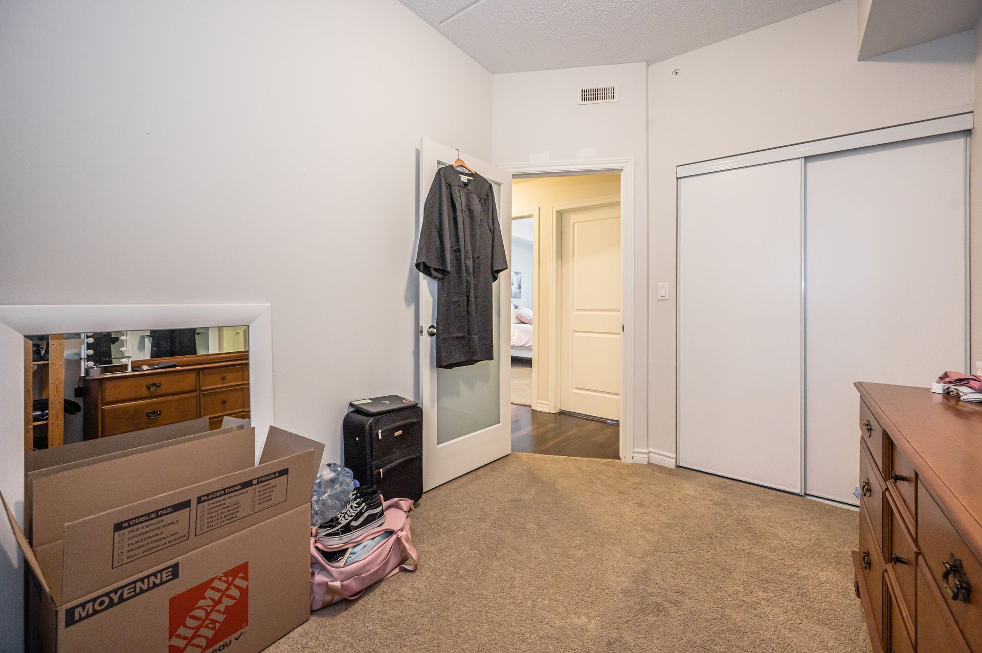 Small bedroom with white closet doors, open doorway, and moving boxes on the floor.