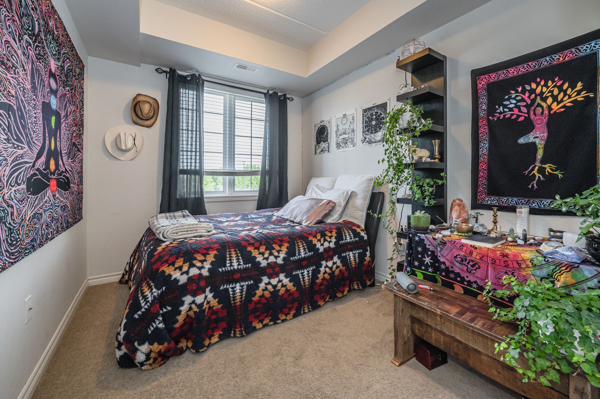 Colorful bedroom with patterned bedspread, window, wall art, and a wooden bench with plants.