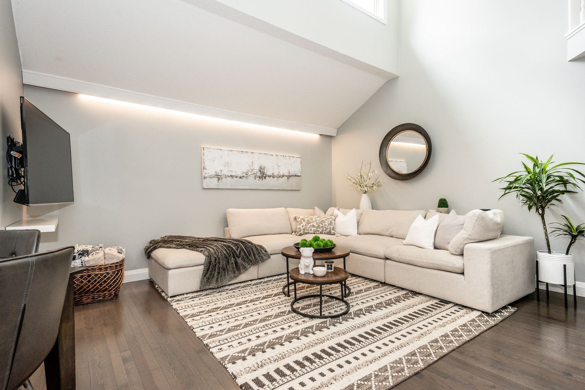 Bright modern living room with beige sectional, patterned rug, round mirror, and skylight。