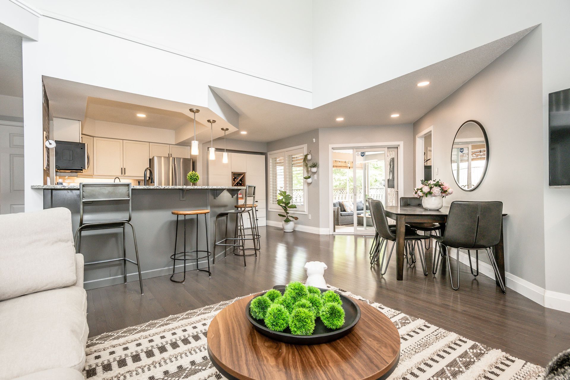 Open-concept modern living and dining room with kitchen, gray chairs, and bright natural light
