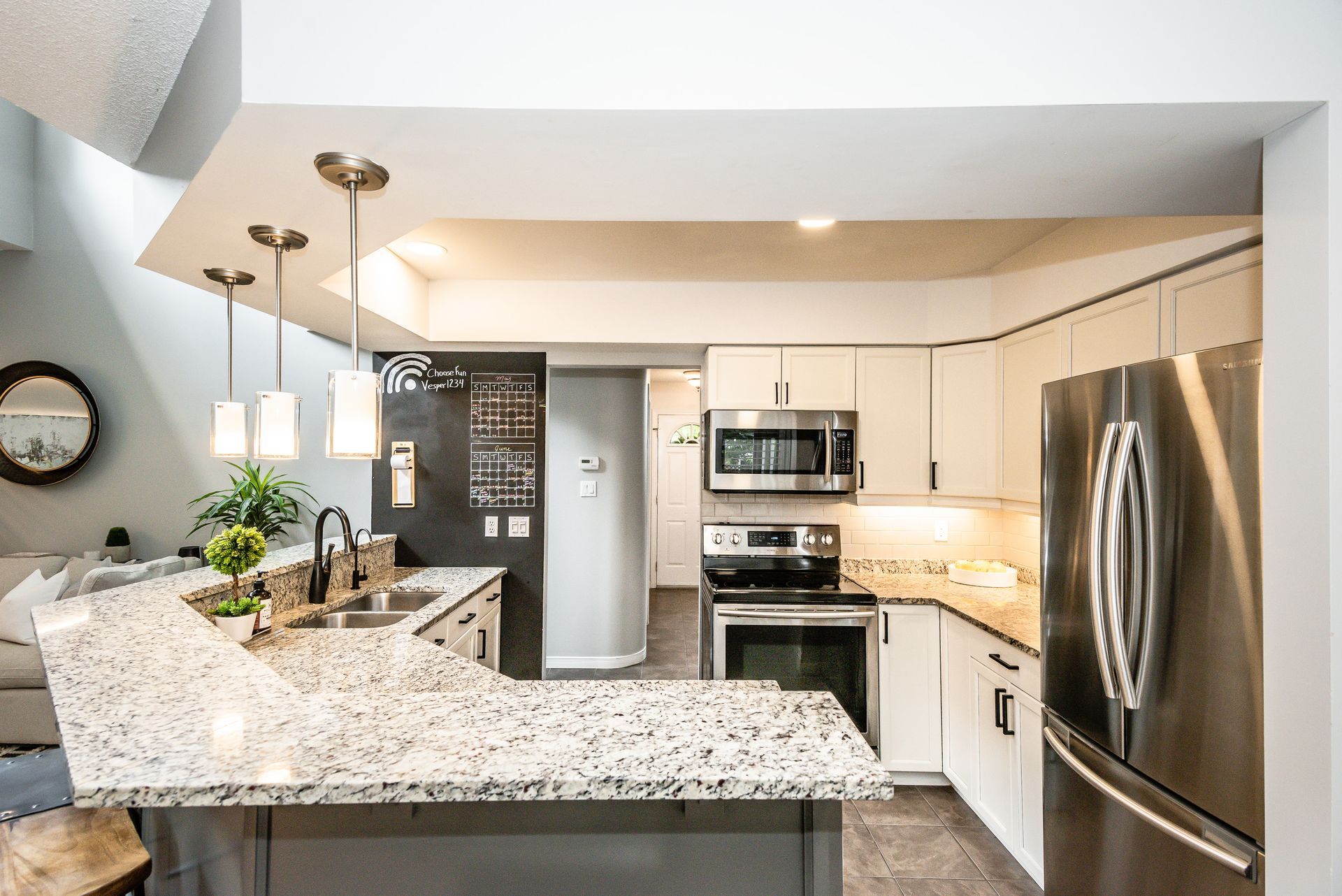 Bright modern kitchen with granite island, white cabinets, stainless steel appliances, and pendant lights