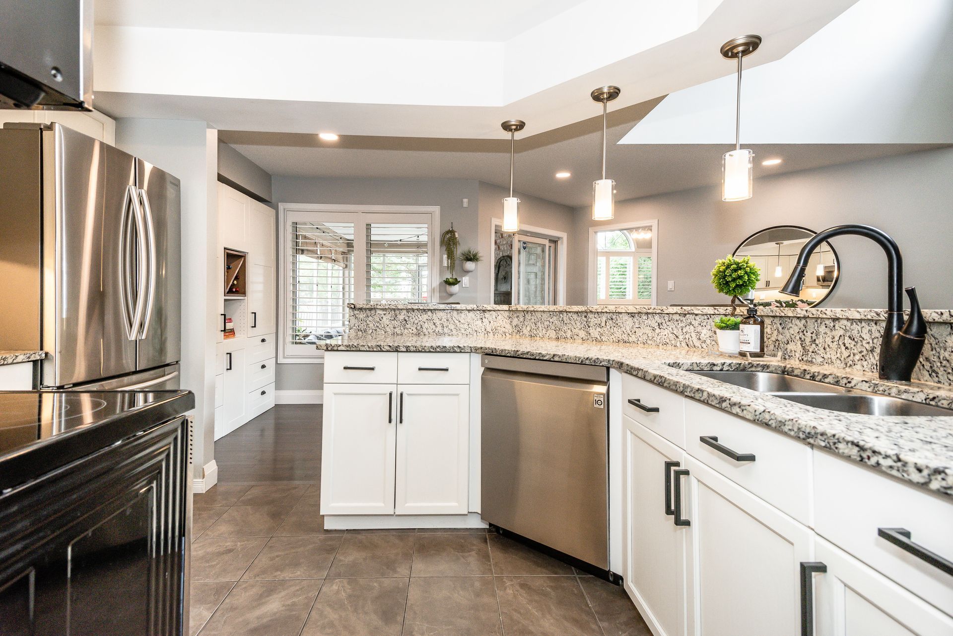 Bright modern kitchen with white cabinets, granite counters, stainless appliances, and pendant lights