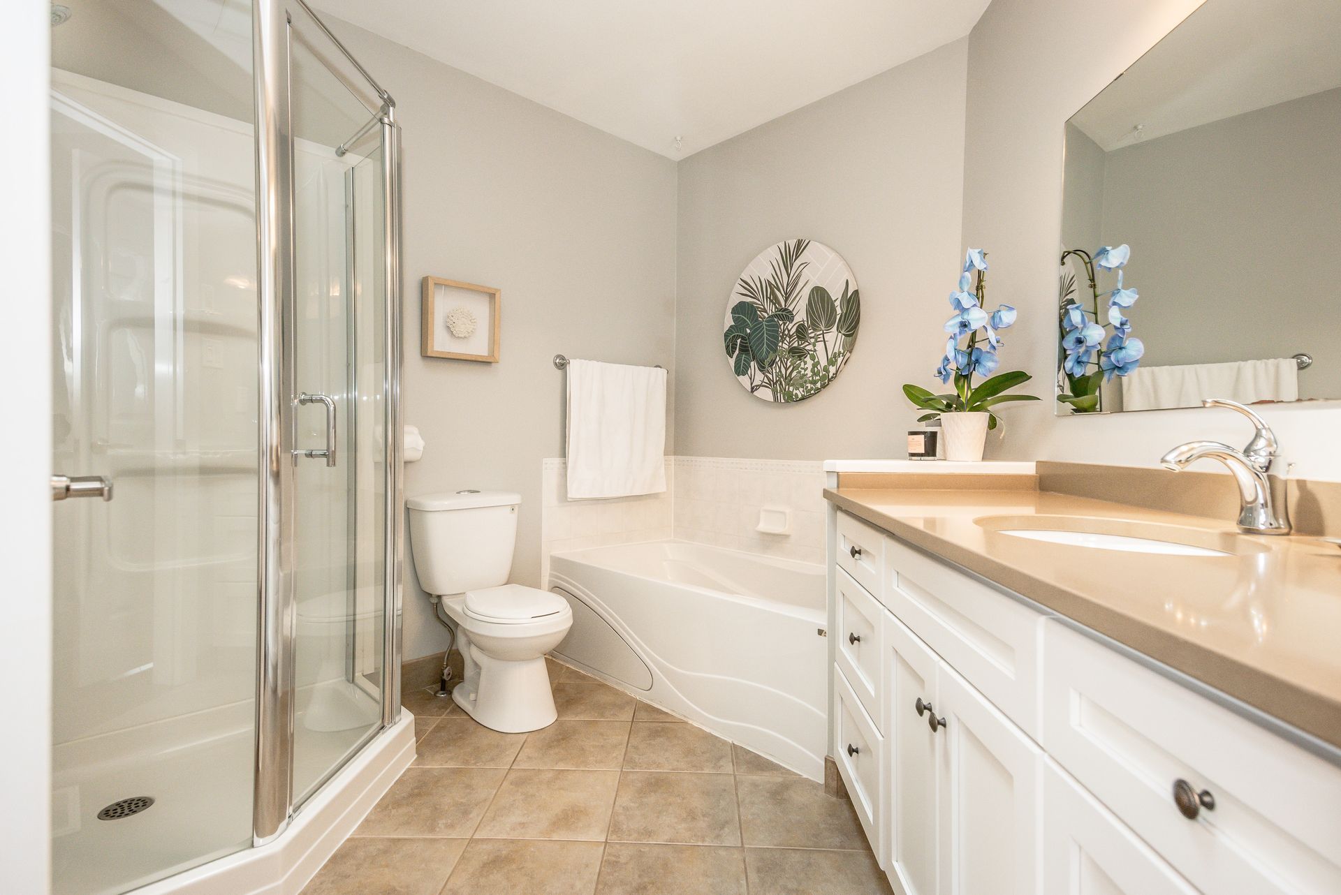 Bright bathroom with glass shower, toilet, bathtub, and white vanity with large mirror.