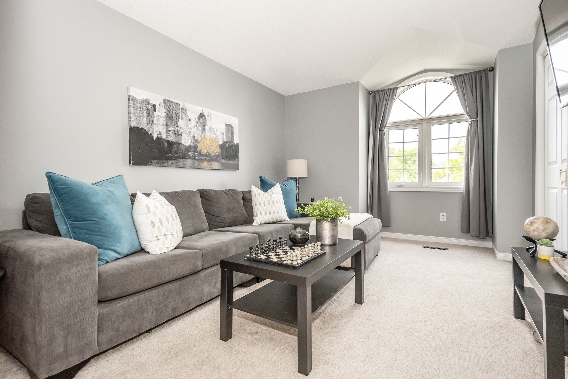 Gray living room with sofa, coffee table, wall art, and large window with curtains